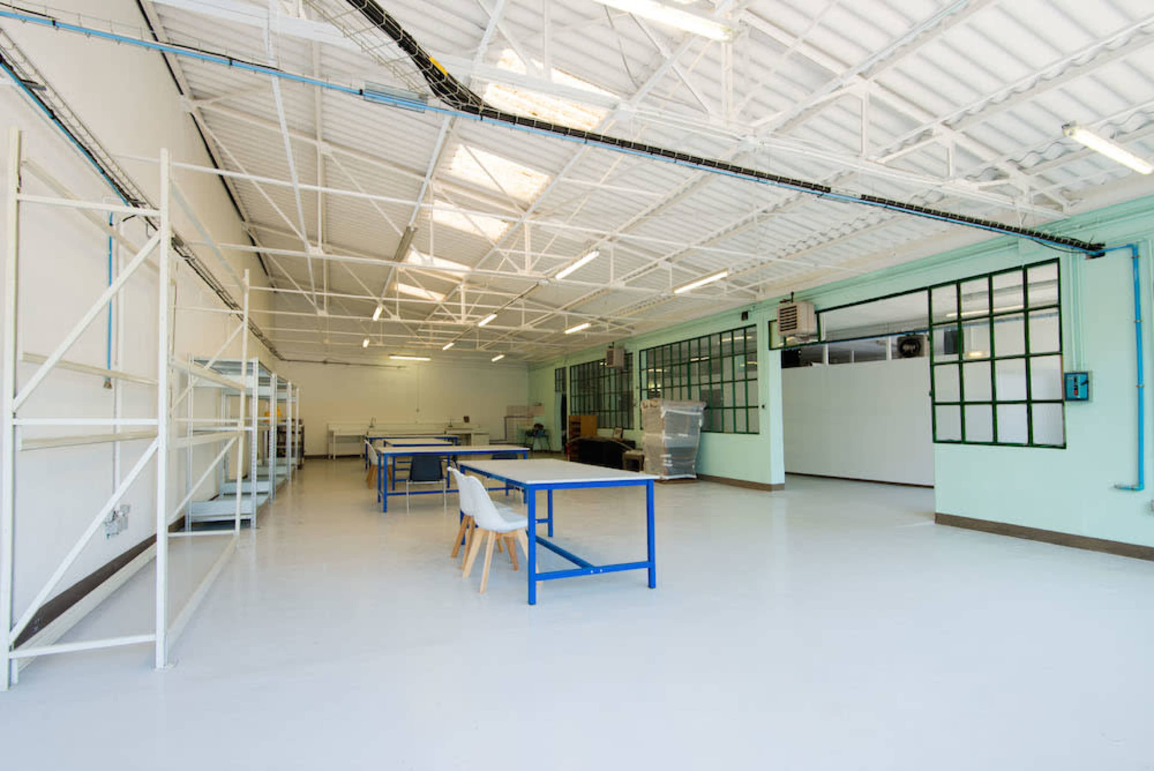 The image shows a spacious, well-lit room with high ceilings, featuring several tables and shelves against the walls.