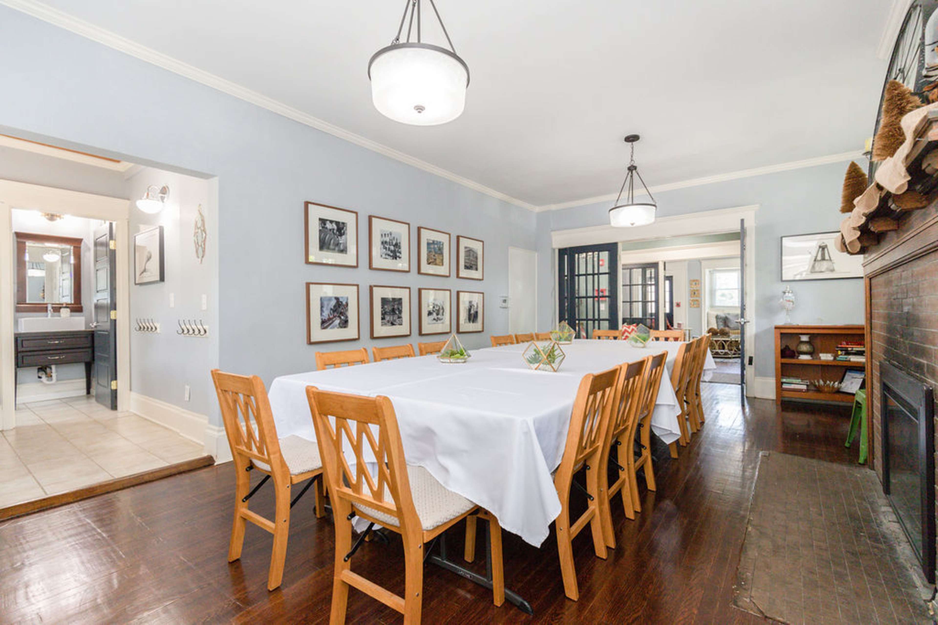 A long dining table is set in a light blue room with framed black-and-white photographs on the walls and a fireplace on one side.