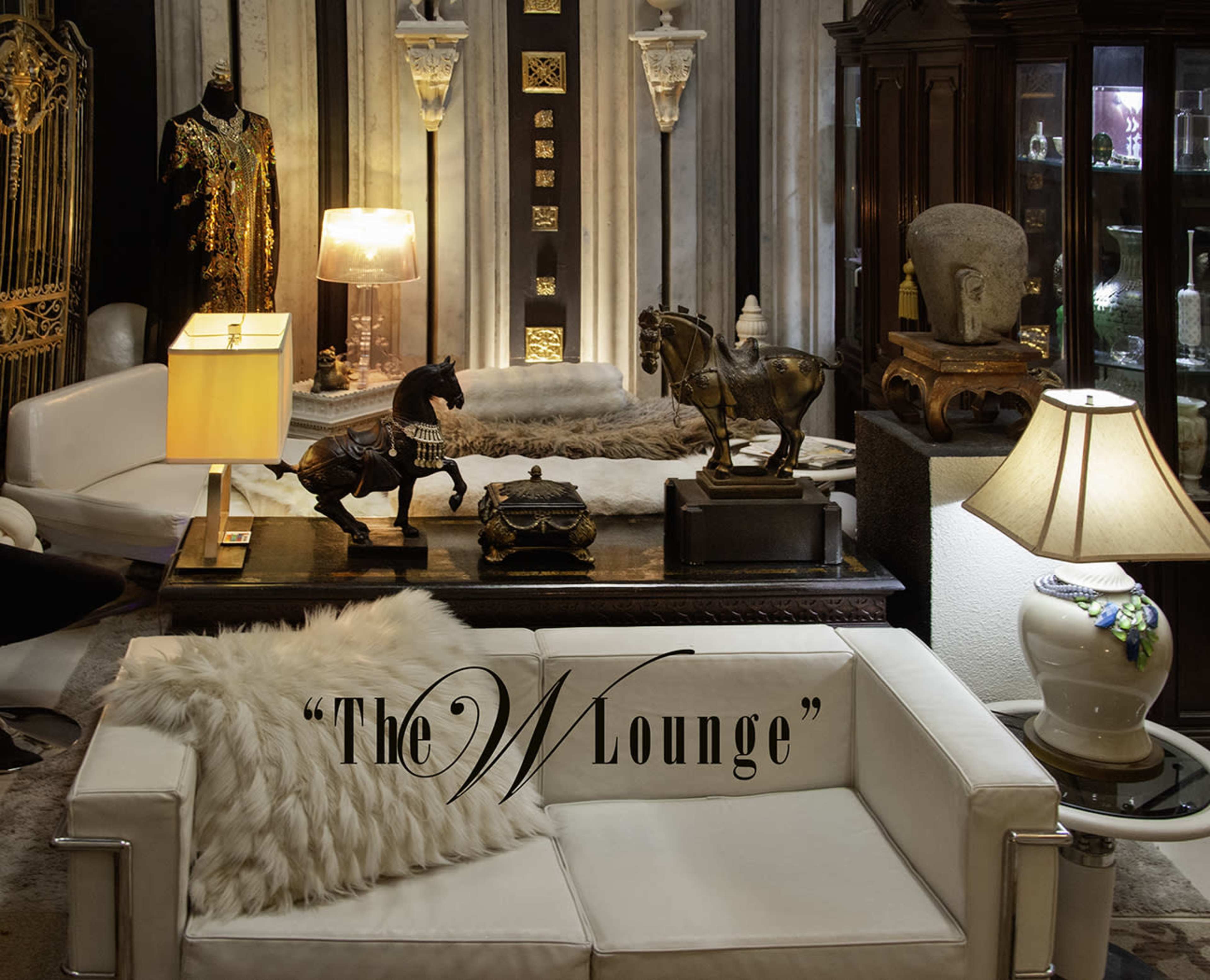 The image shows a well-furnished lounge area with a white sofa, decorative lamps, and ornamental objects including horse figurines and sculptures.