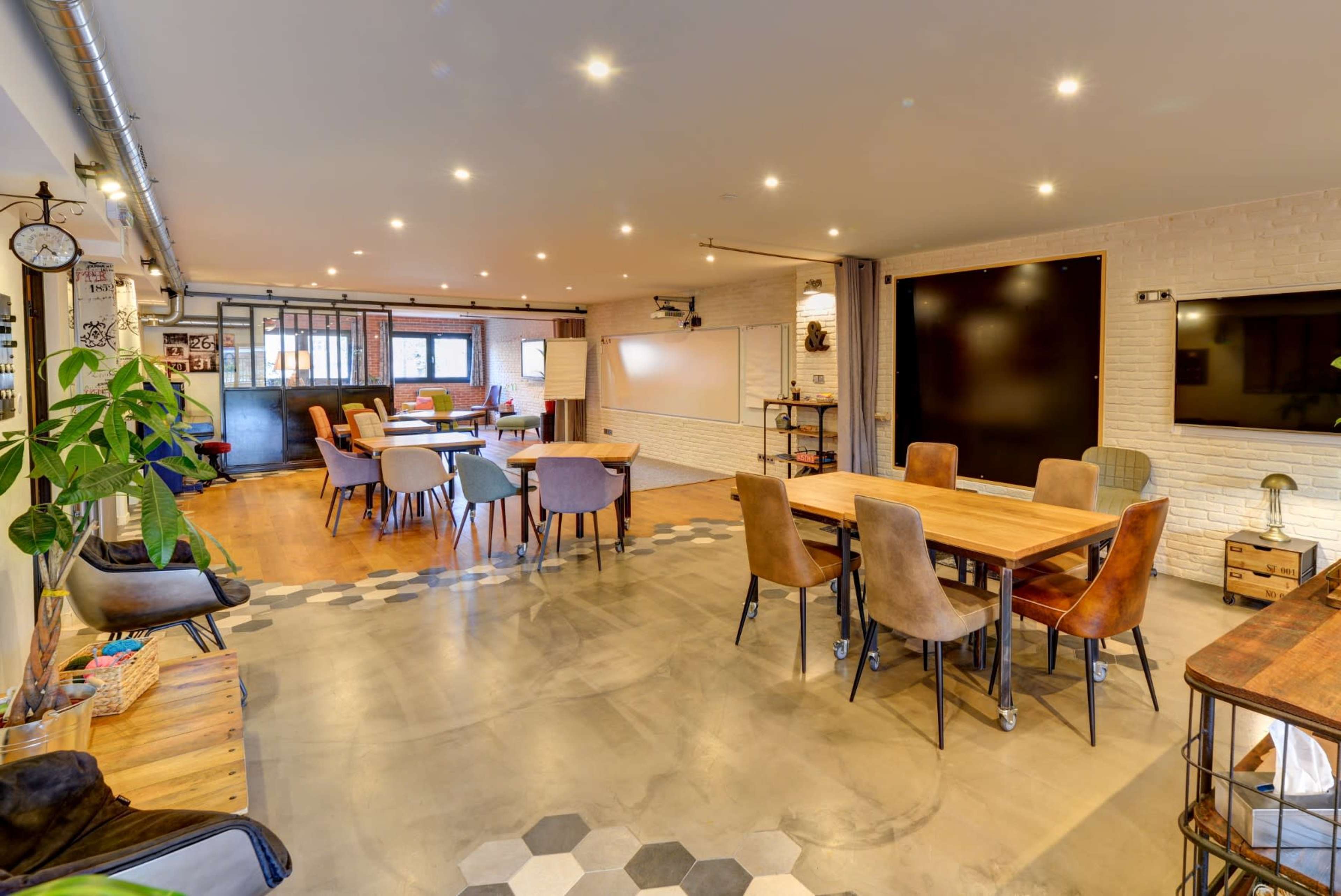A modern workspace with various tables and chairs arranged around a large open area, complemented by white walls and wooden accents.