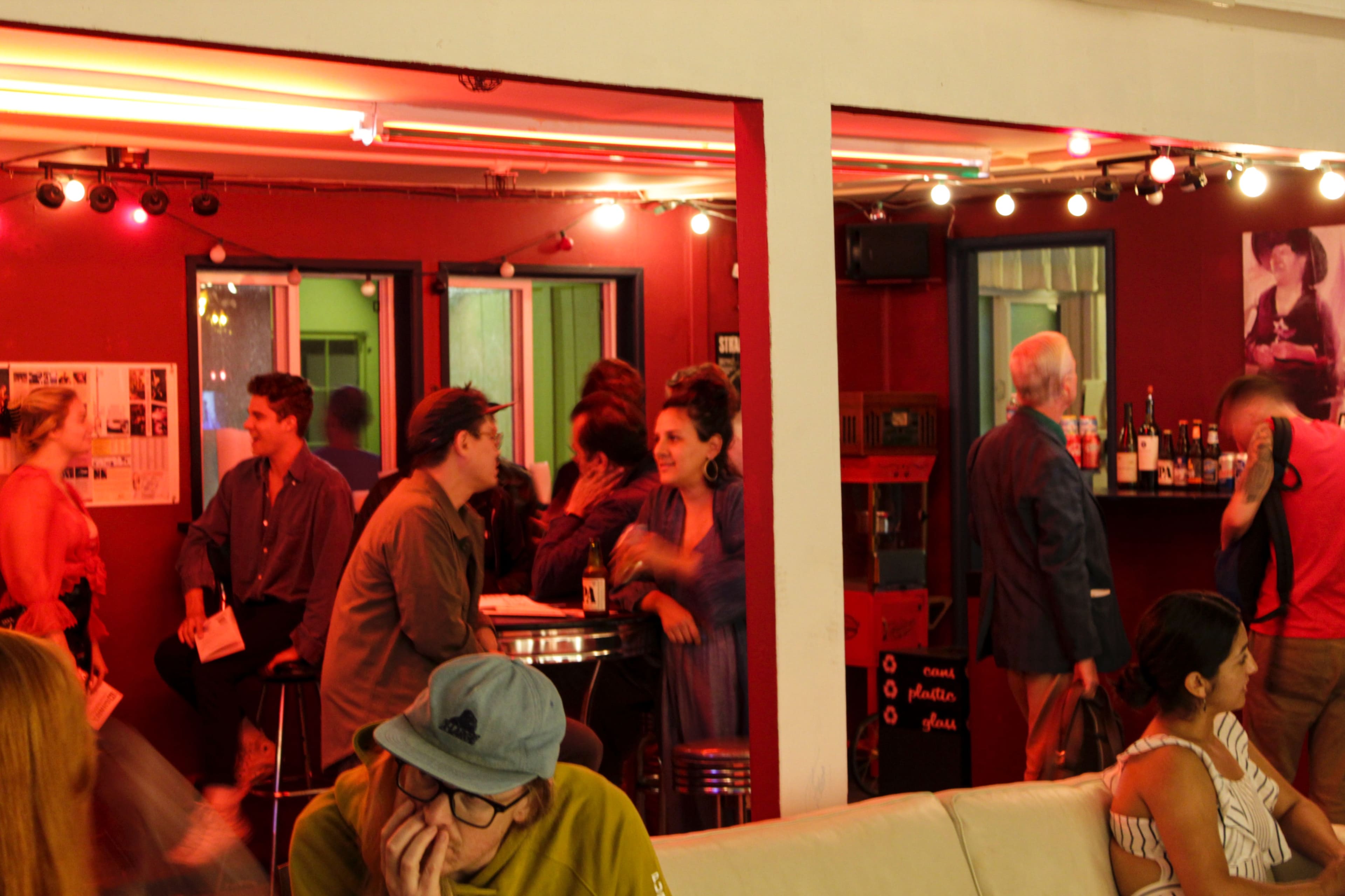 A lively social gathering takes place in a dimly lit lounge featuring a bar area and mingling guests.