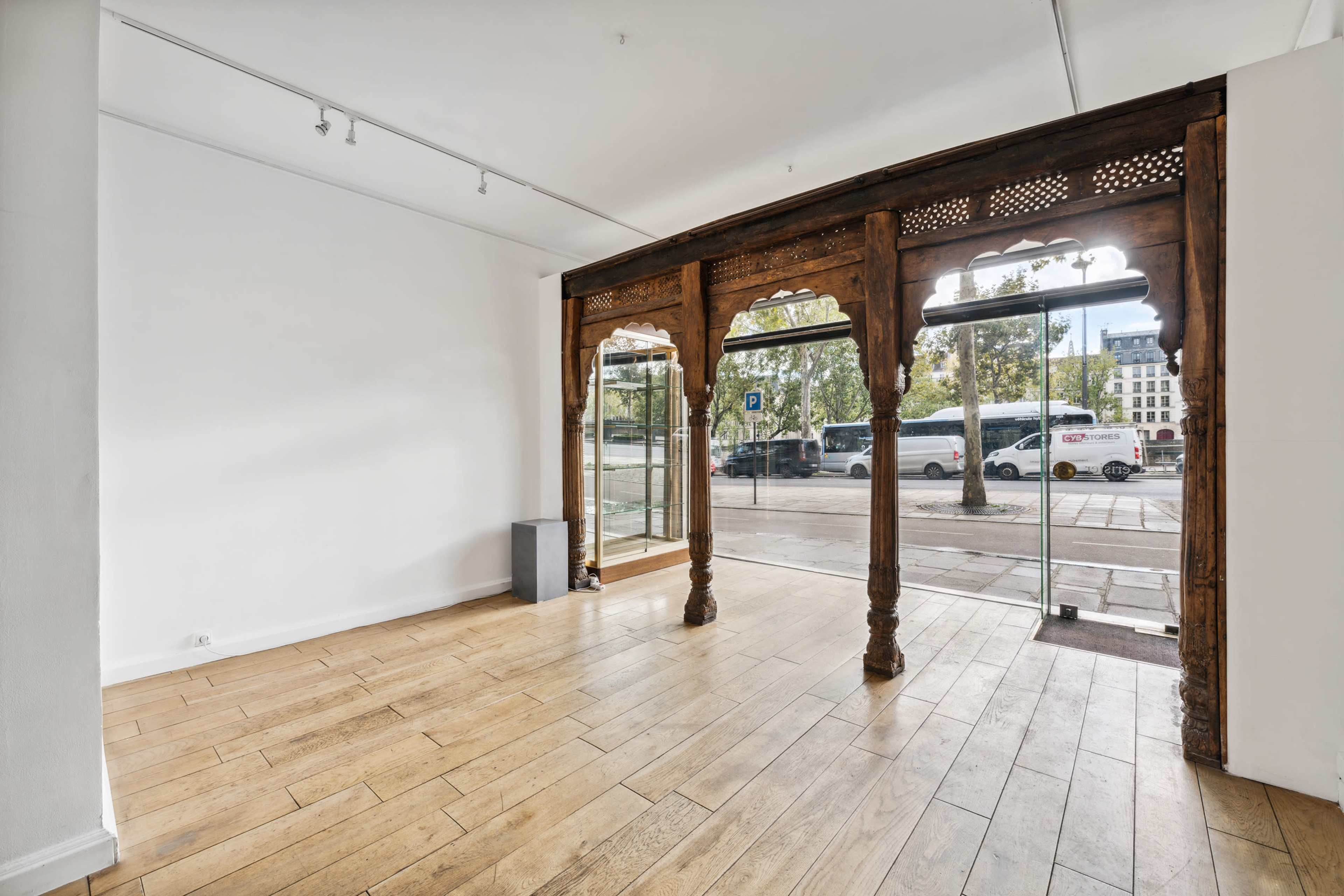 The image shows a spacious, unfurnished interior with wooden flooring and a large glass entrance framed by intricate wooden arches.