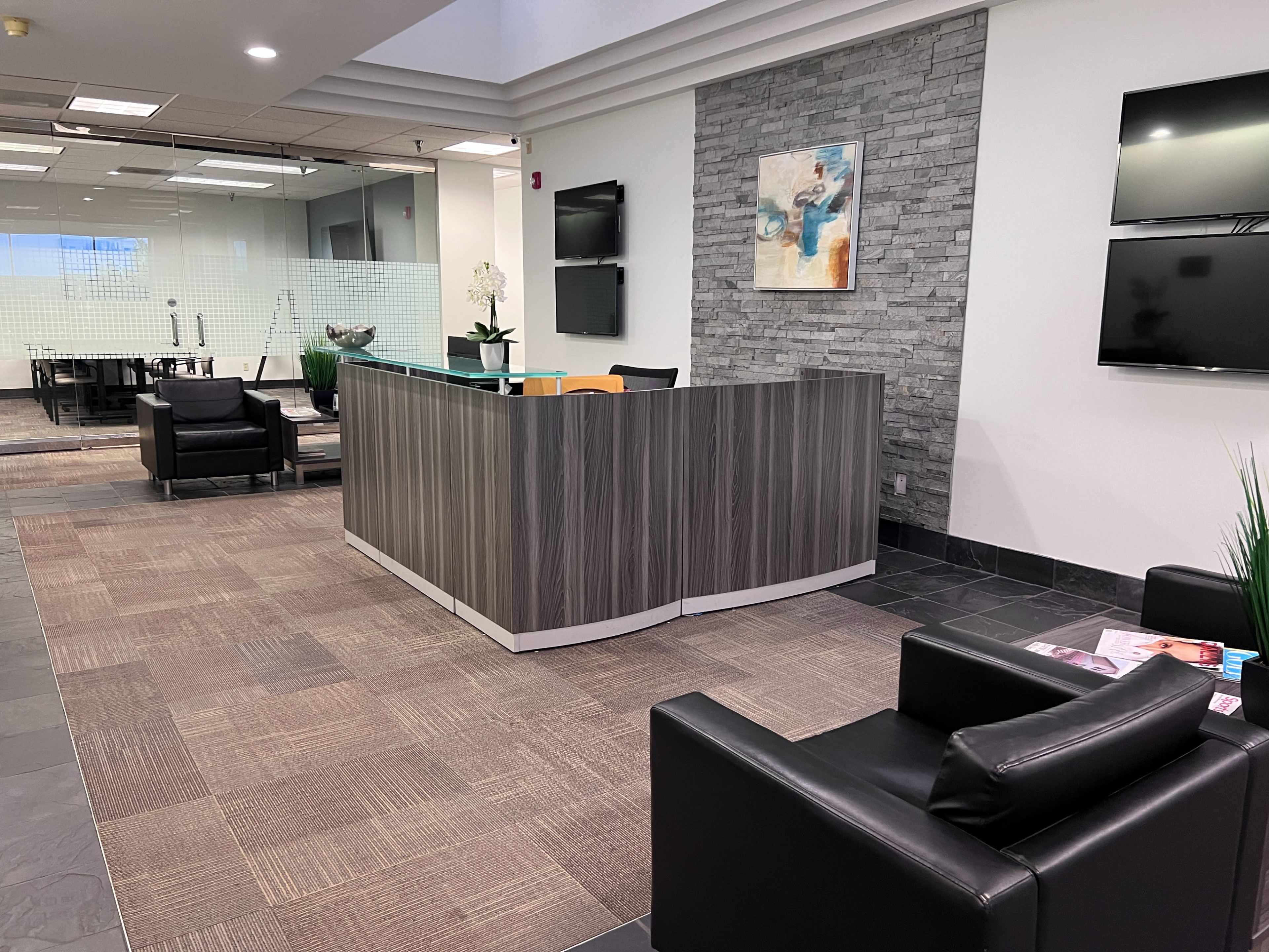 A modern office reception area with a wooden front desk, black chairs, and a stone accent wall.