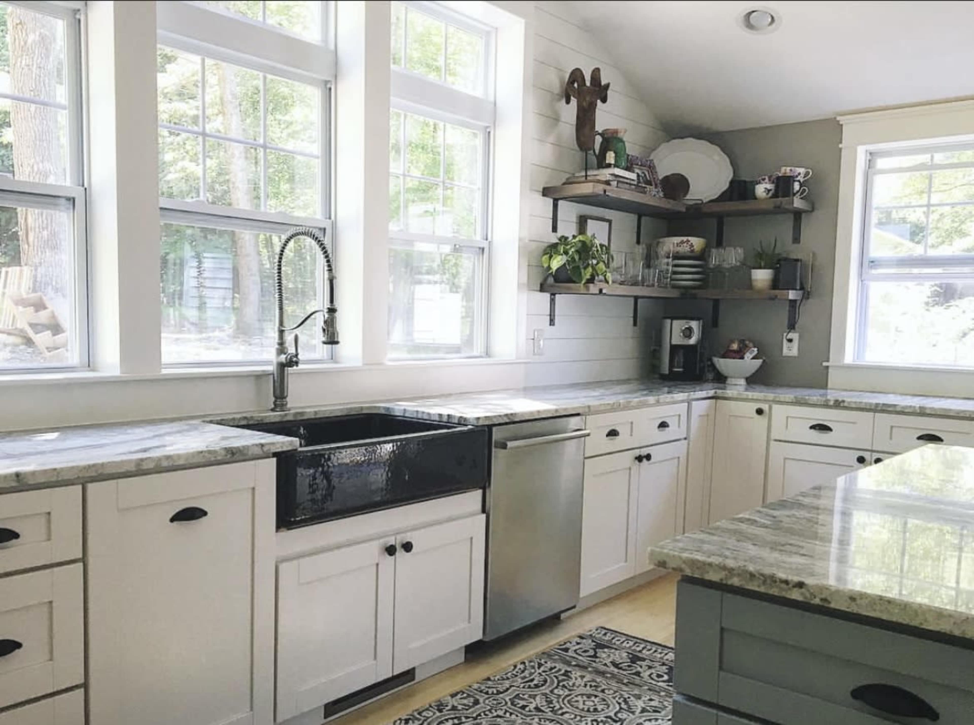 A kitchen features white cabinetry, a farmhouse sink, stainless steel appliances, and large windows that provide natural light.