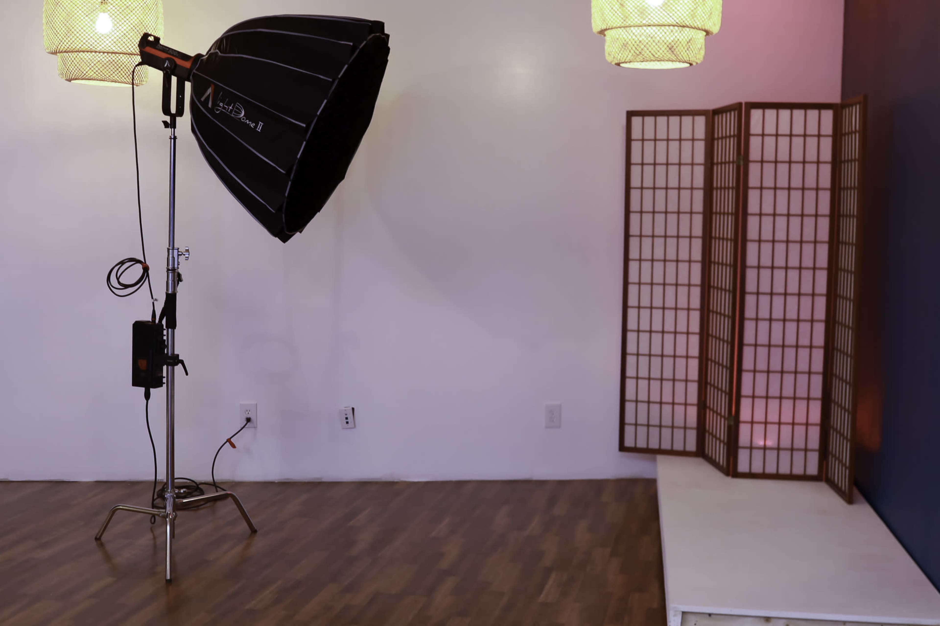 The image shows a photography studio with a large softbox light, a folding screen, and a wooden floor.
