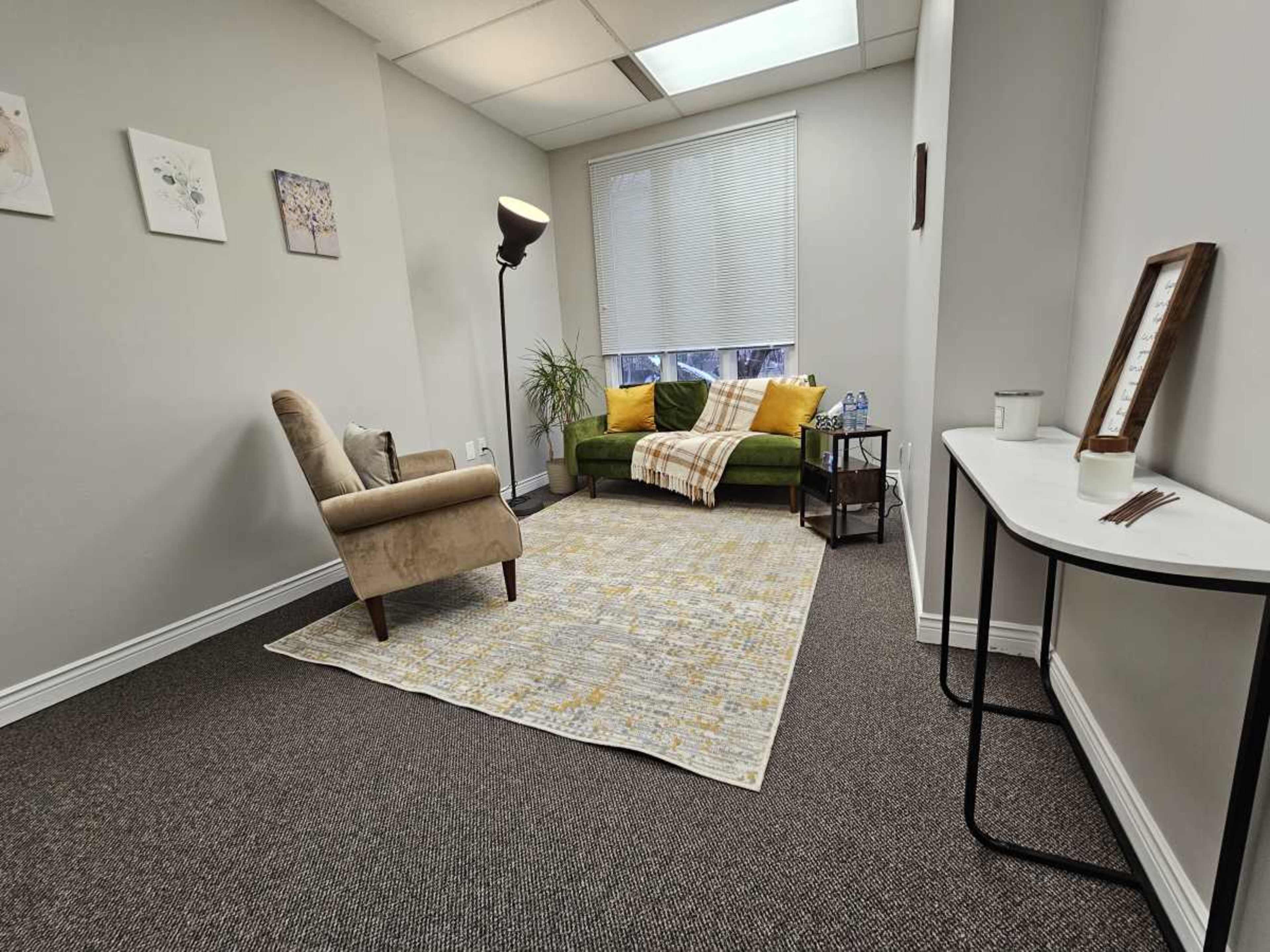 The image shows a well-lit room with a green couch, an armchair, a small side table, and a rug on the carpeted floor.