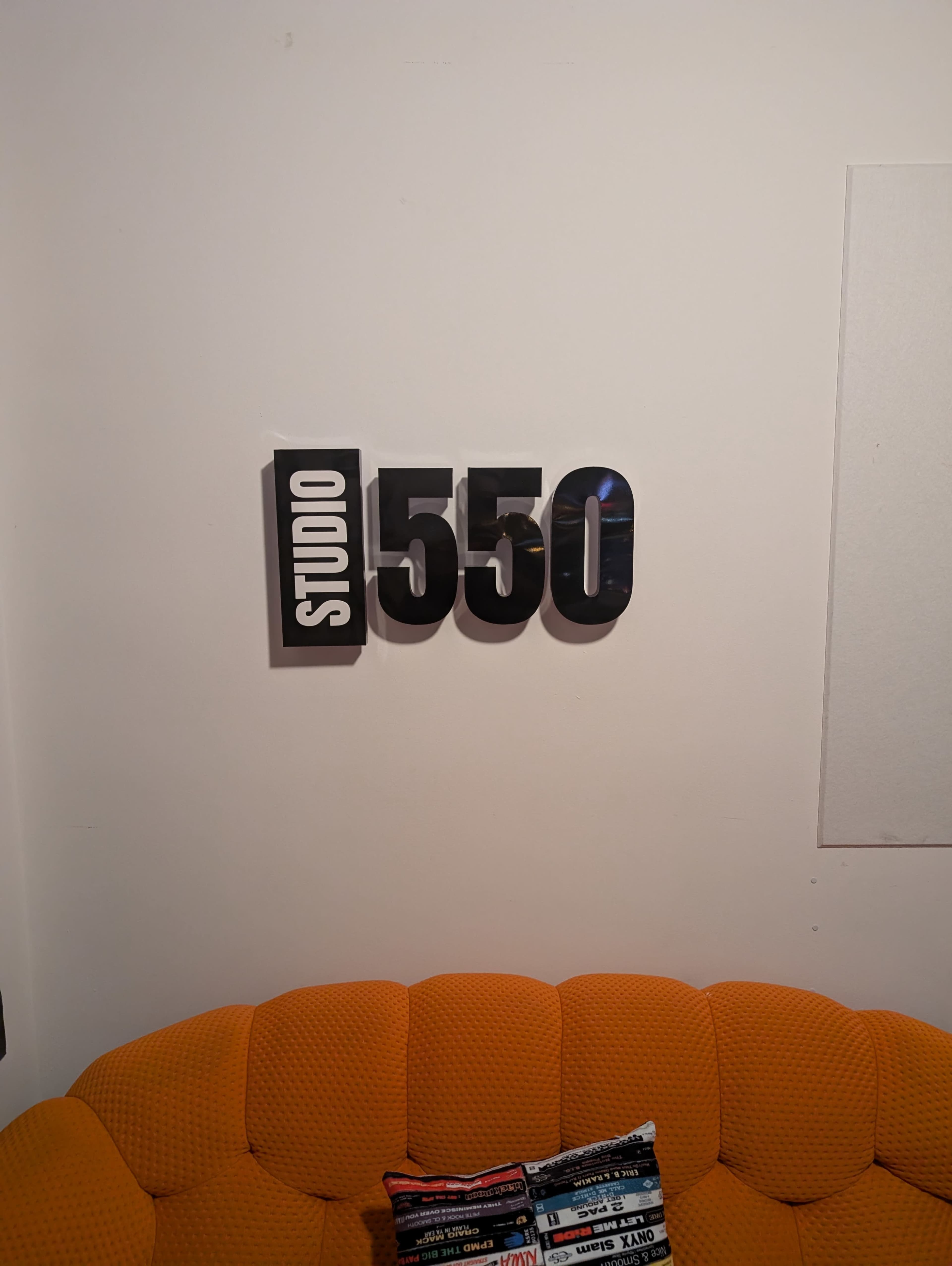 The image shows a bright orange, circular couch with a decorative pillow, and a sign on the wall above it that reads "STUDIO 550."