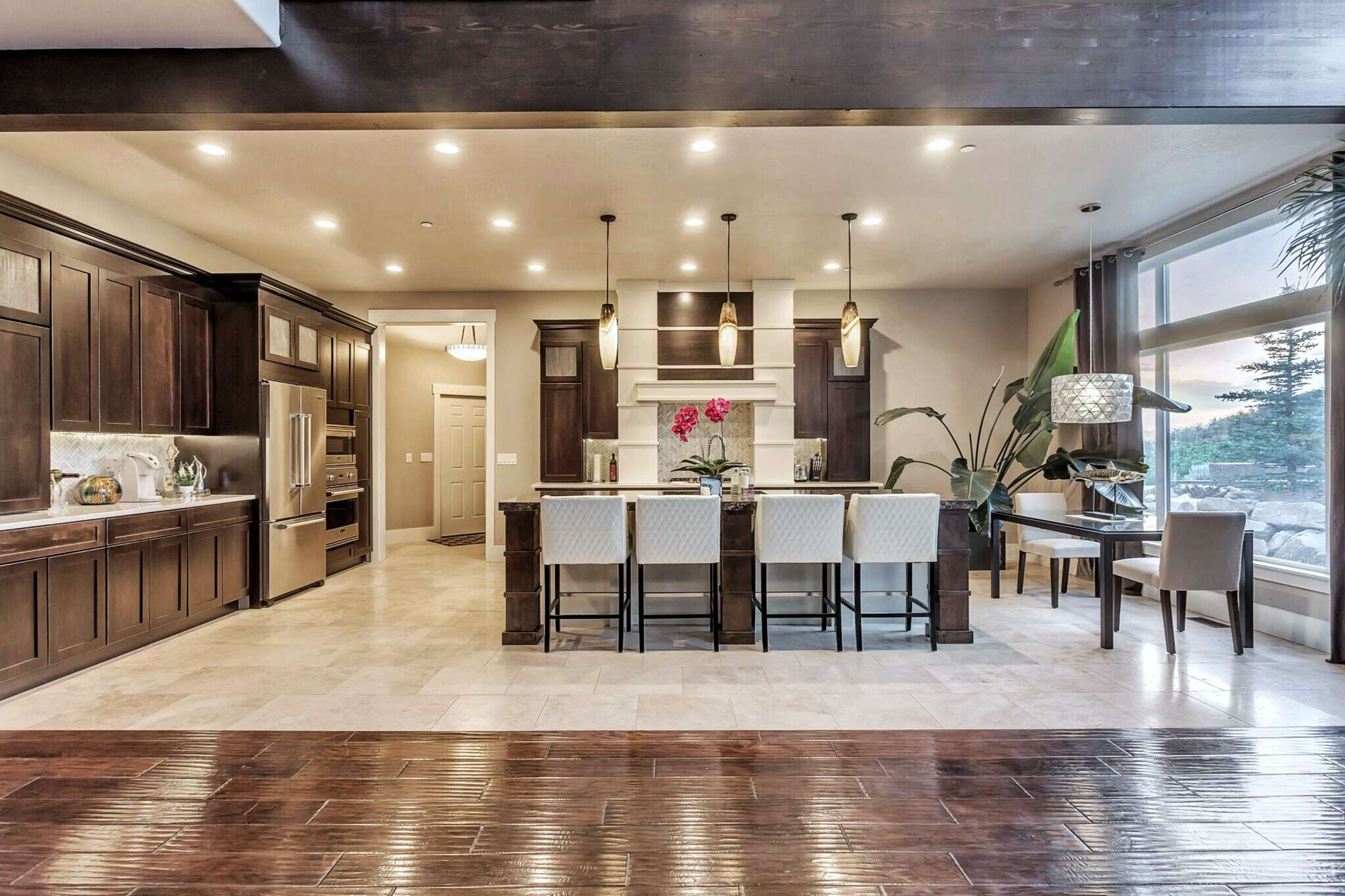 A modern kitchen features dark wooden cabinetry, a large central island with seating, and bright lighting.