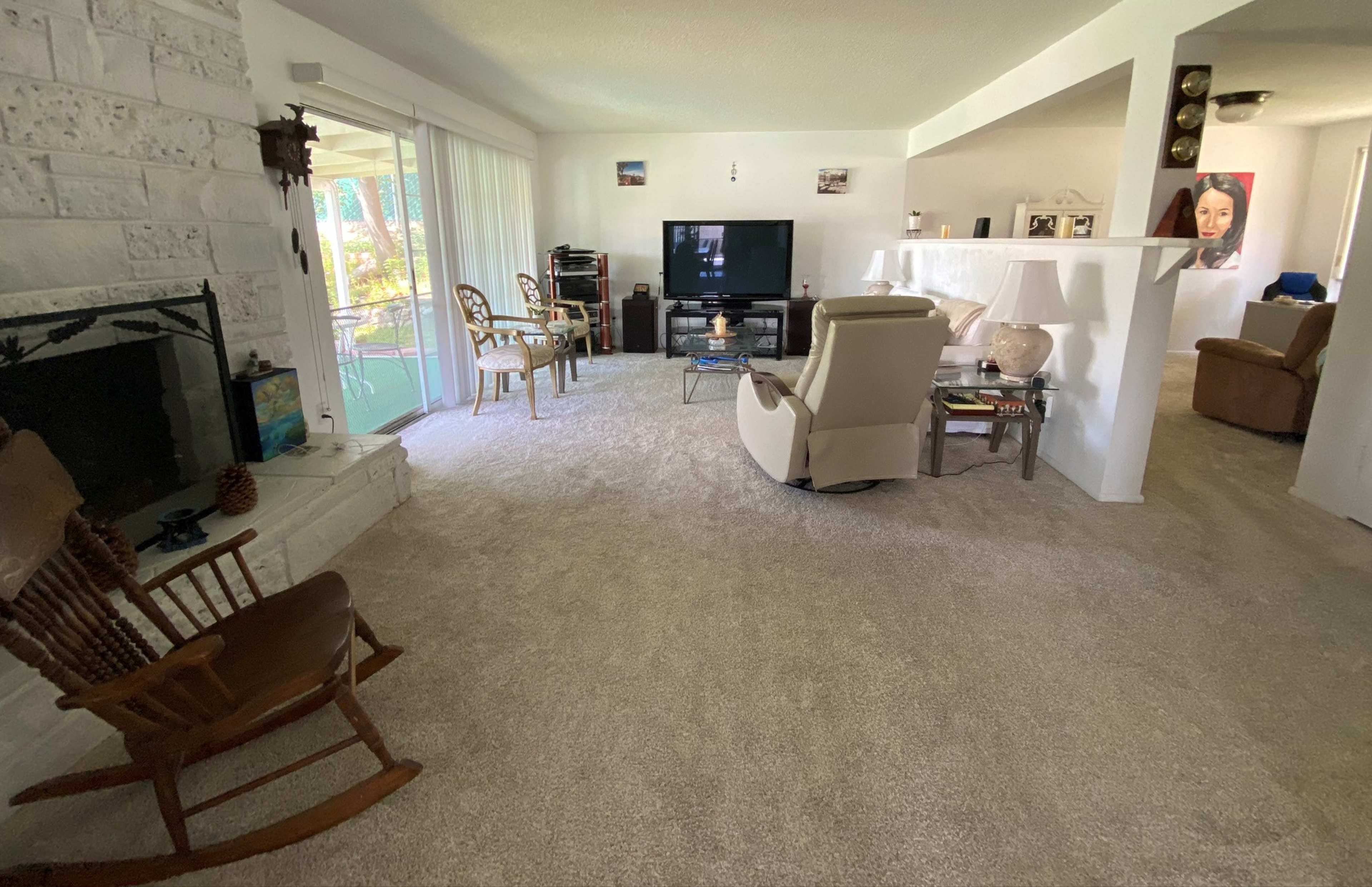A spacious living room with a fireplace, a television, various seating options, and soft carpeting.