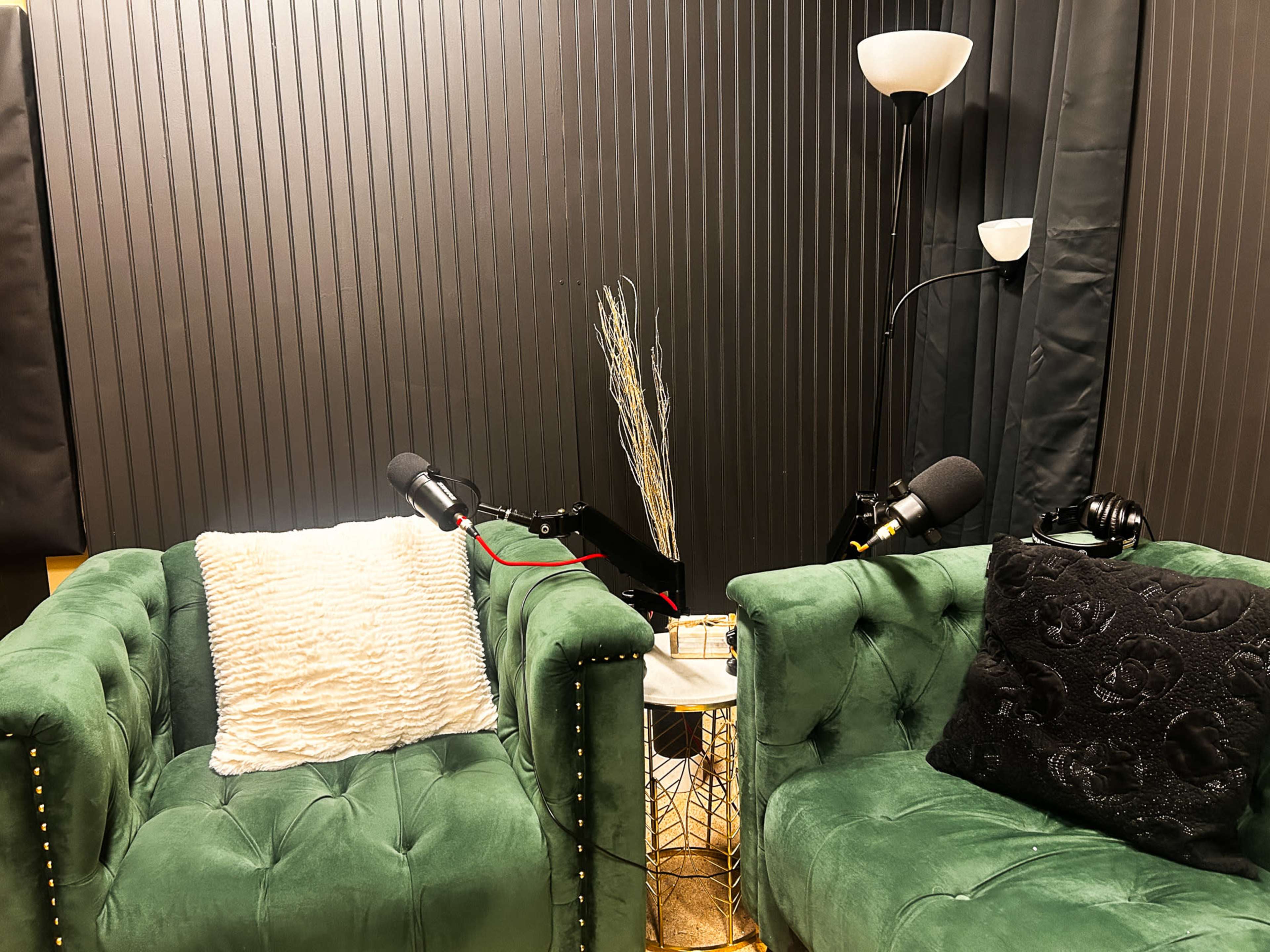 The image shows a recording studio setup with two green velvet chairs, a small table with a decorative item, and two microphones on stands nearby.