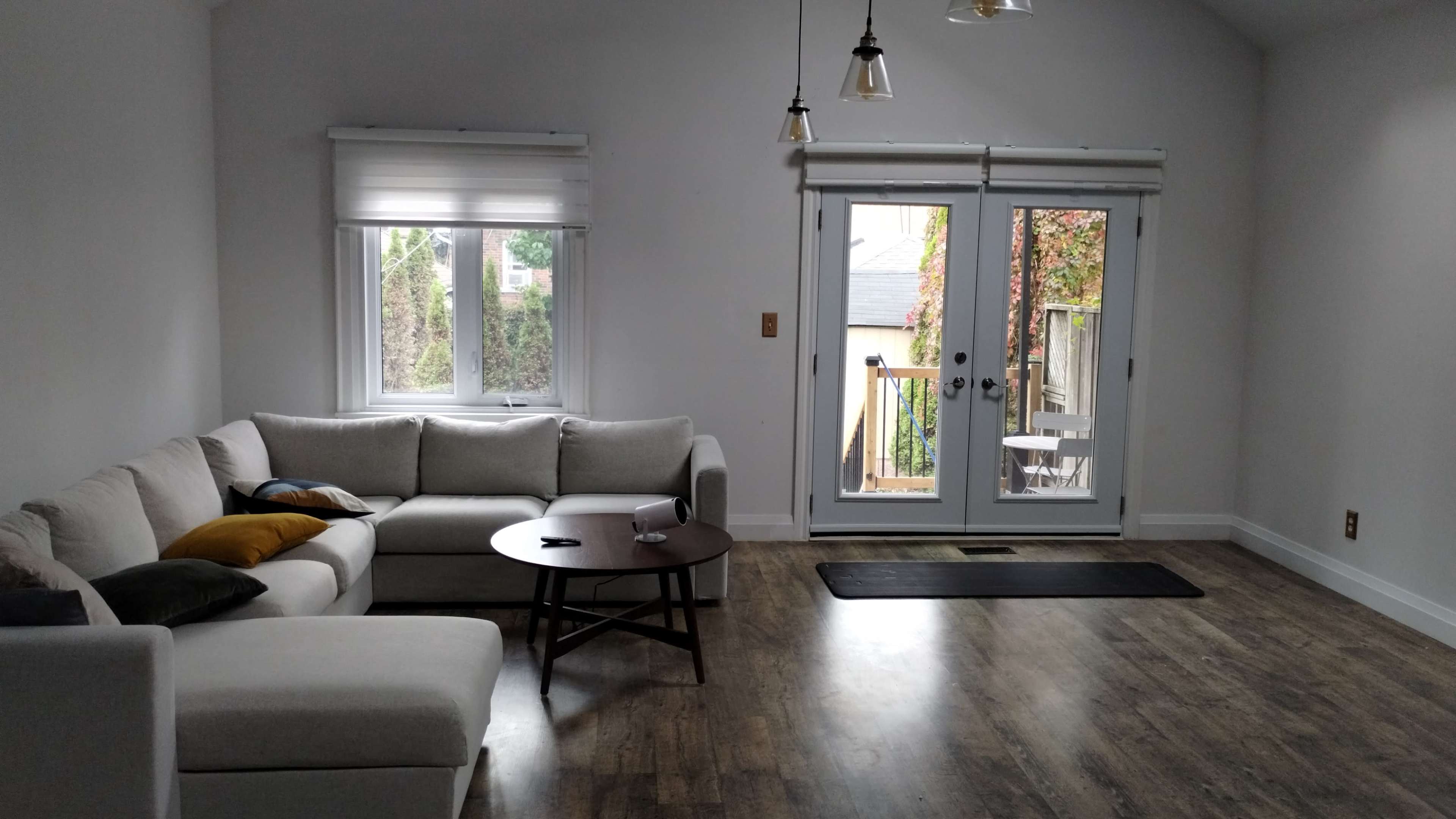 A light-filled living room features a sectional sofa, a round table, and access to a small outdoor deck through double doors.