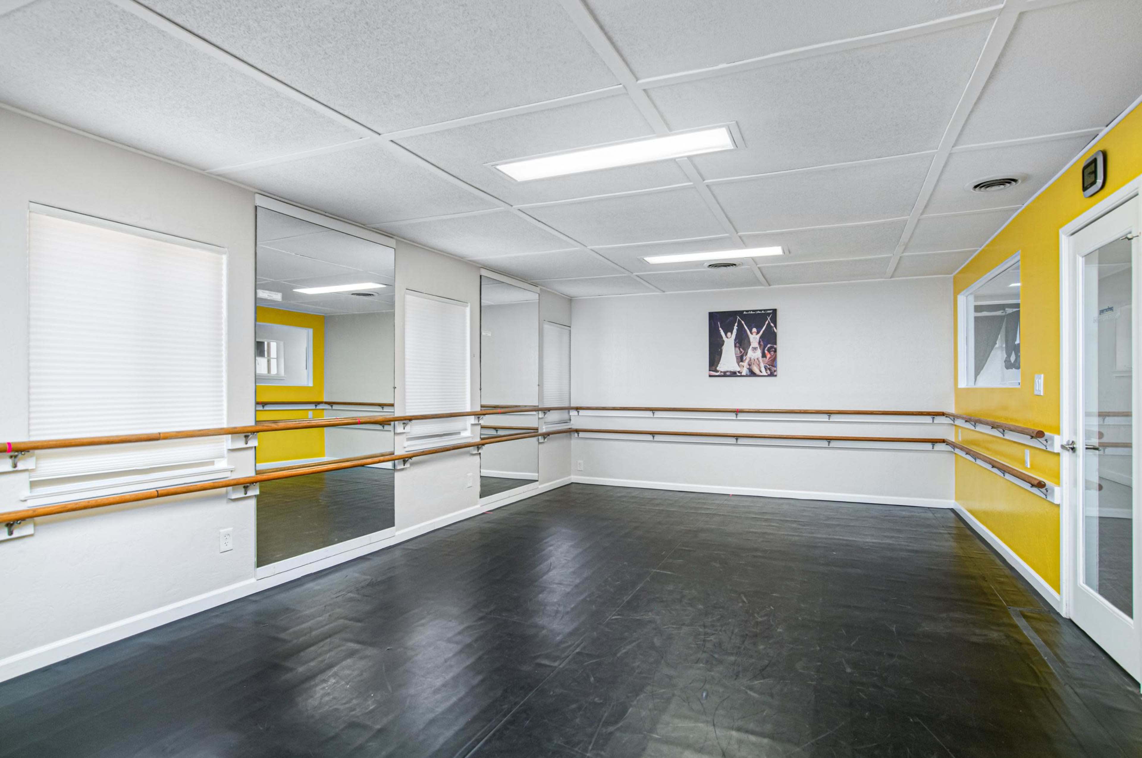A well-lit dance studio features mirrored walls, black flooring, and a bright yellow accent wall.