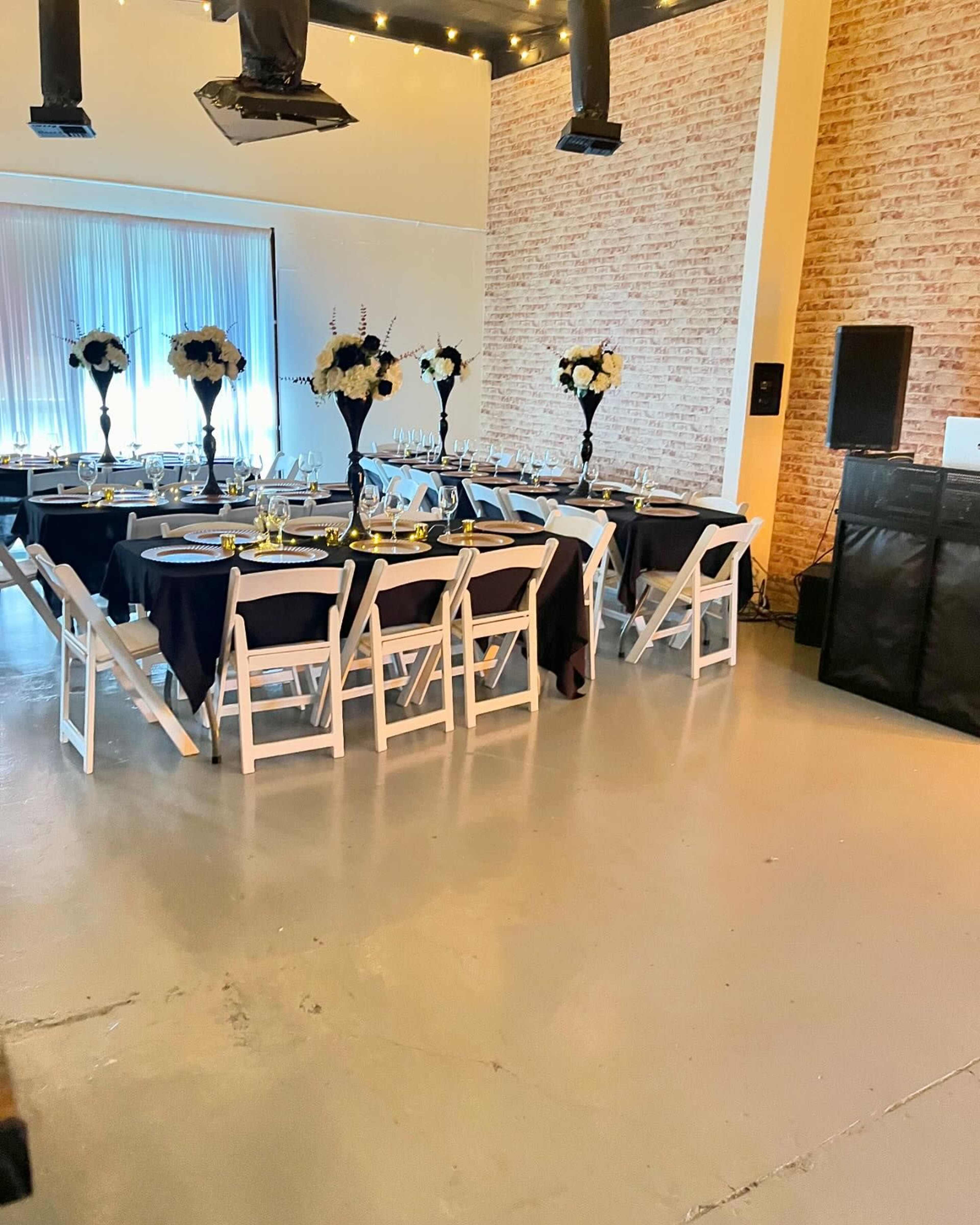 A dining area featuring black and white table settings, elegant flower centerpieces, and rows of white chairs arranged around circular tables.