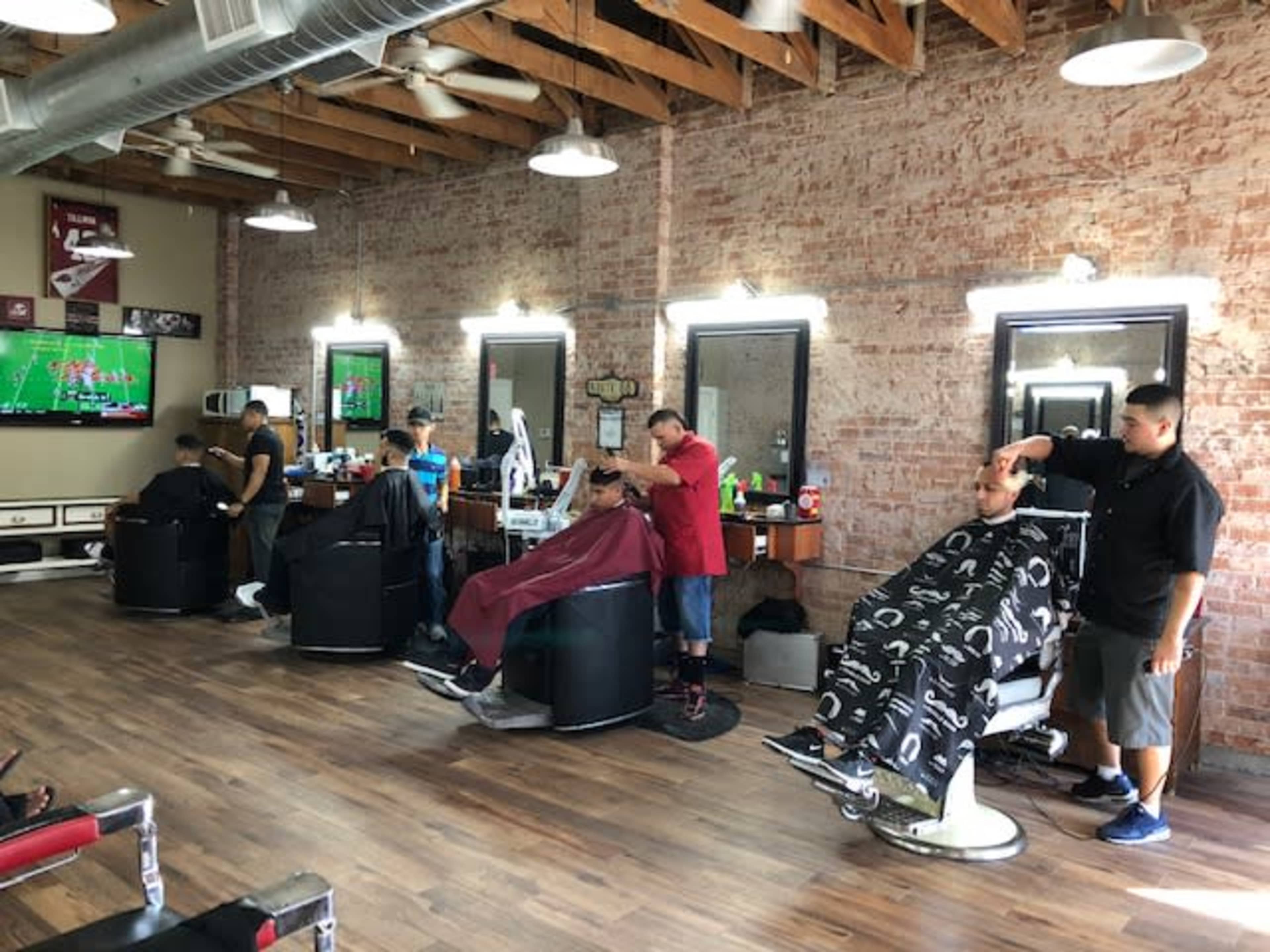 A barbershop with several clients getting haircuts, while barbers work at their stations along a brick wall.