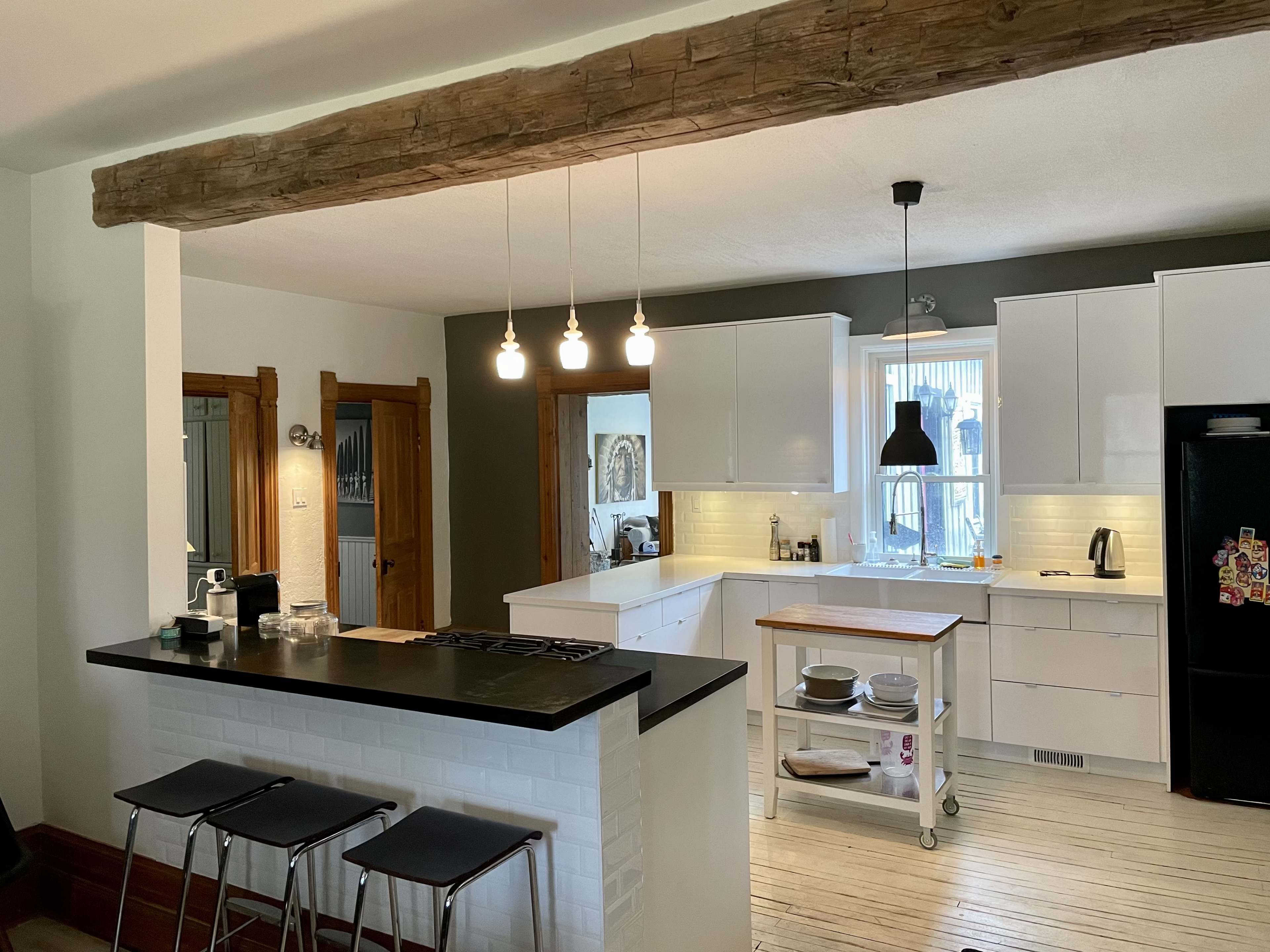 A modern kitchen features white cabinetry, a wooden beam overhead, and a central island with bar stools.