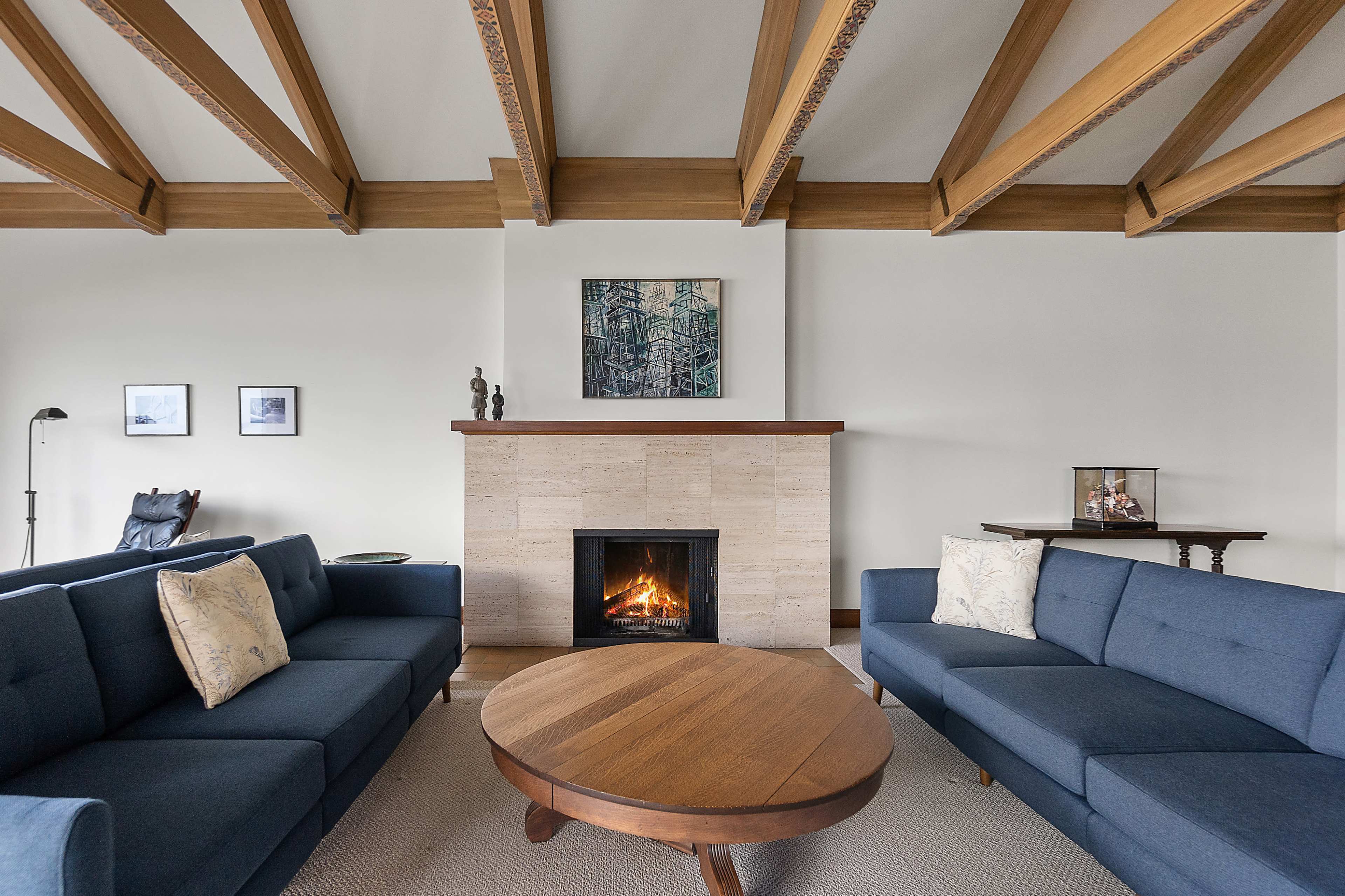The living room features two blue sofas facing each other, a round wooden coffee table in the center, and a stone fireplace with a piece of artwork above it.