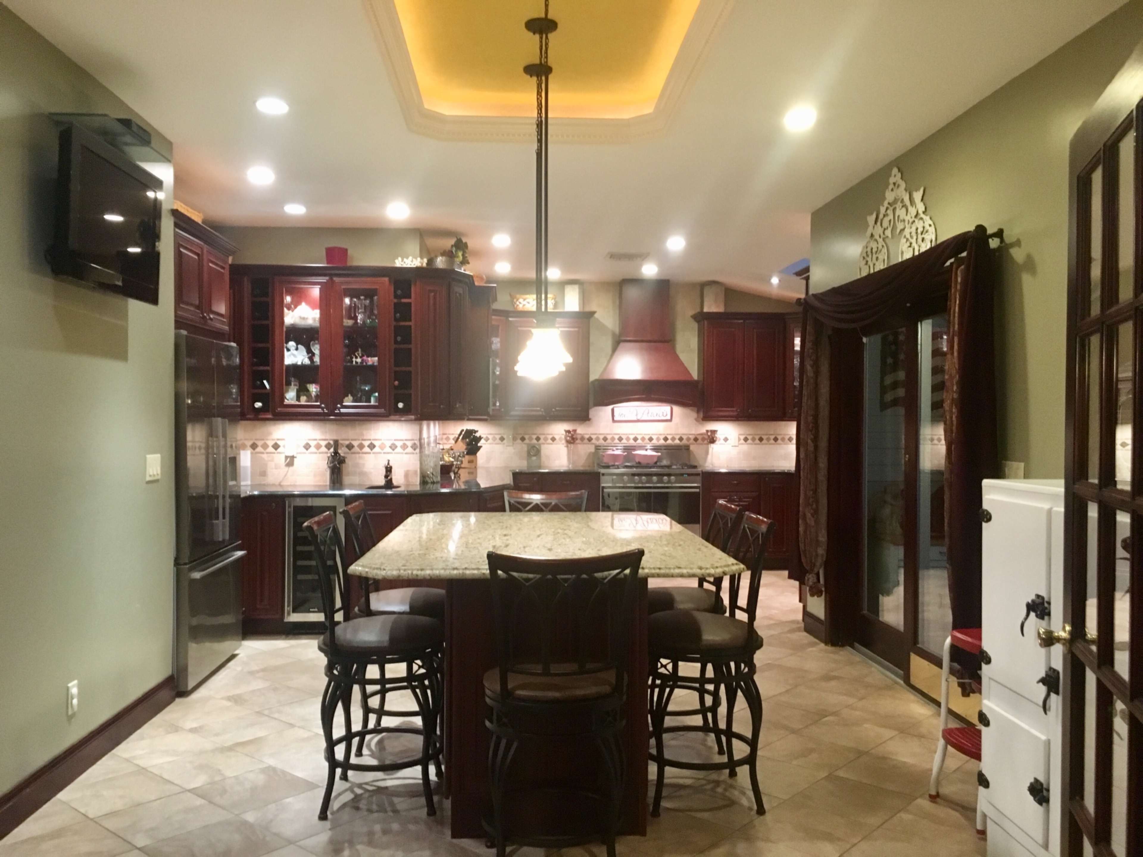 A spacious kitchen with dark wood cabinetry, a large granite island, and modern appliances, featuring warm lighting and tiled flooring.
