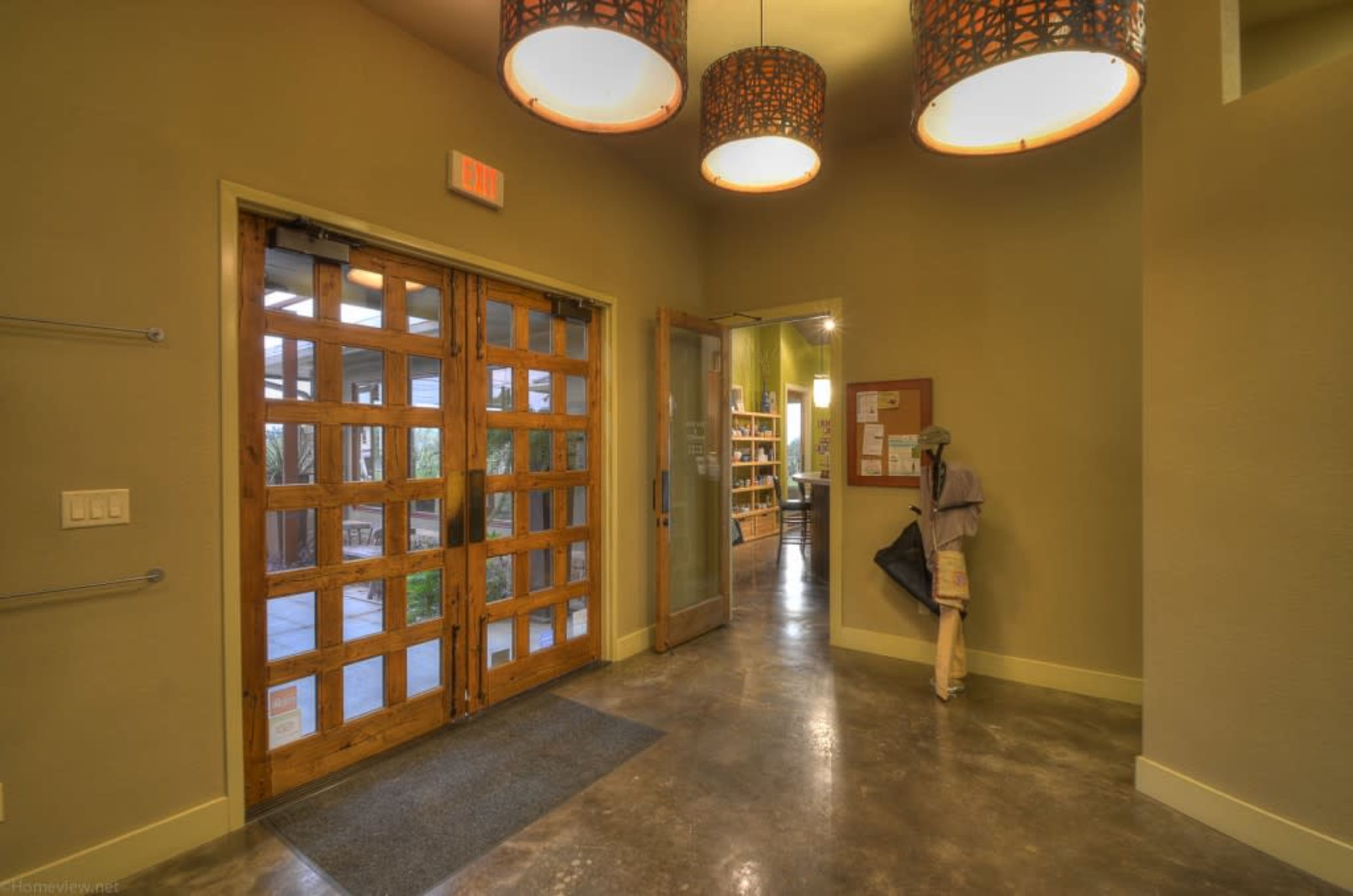 A well-lit entrance area features wooden doors, a gray floor, and a mannequin holding a black object, while shelves are visible in the background.