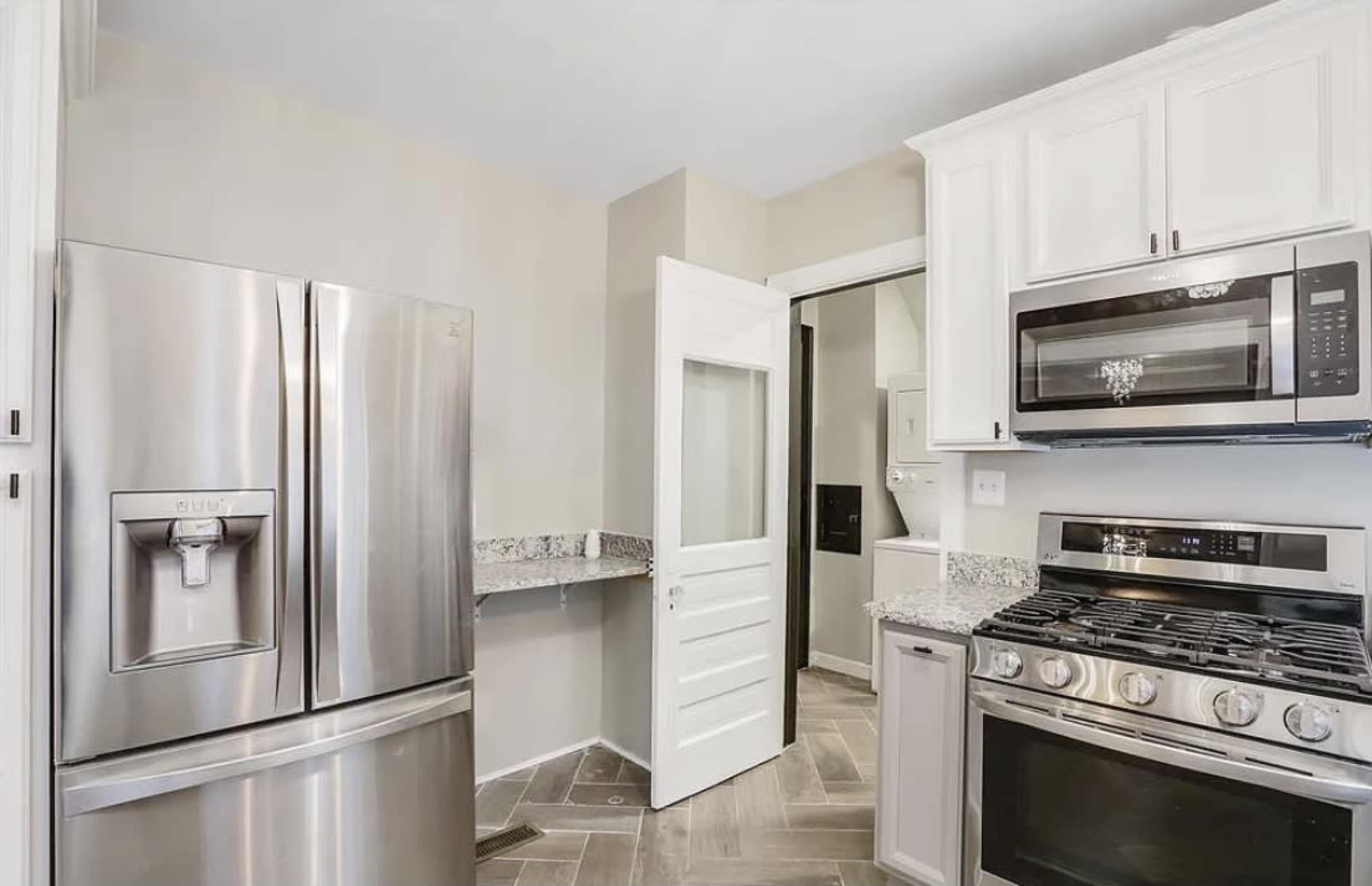 A modern kitchen with stainless steel appliances, including a refrigerator and a gas stove, featuring granite countertops and a light-colored wall.