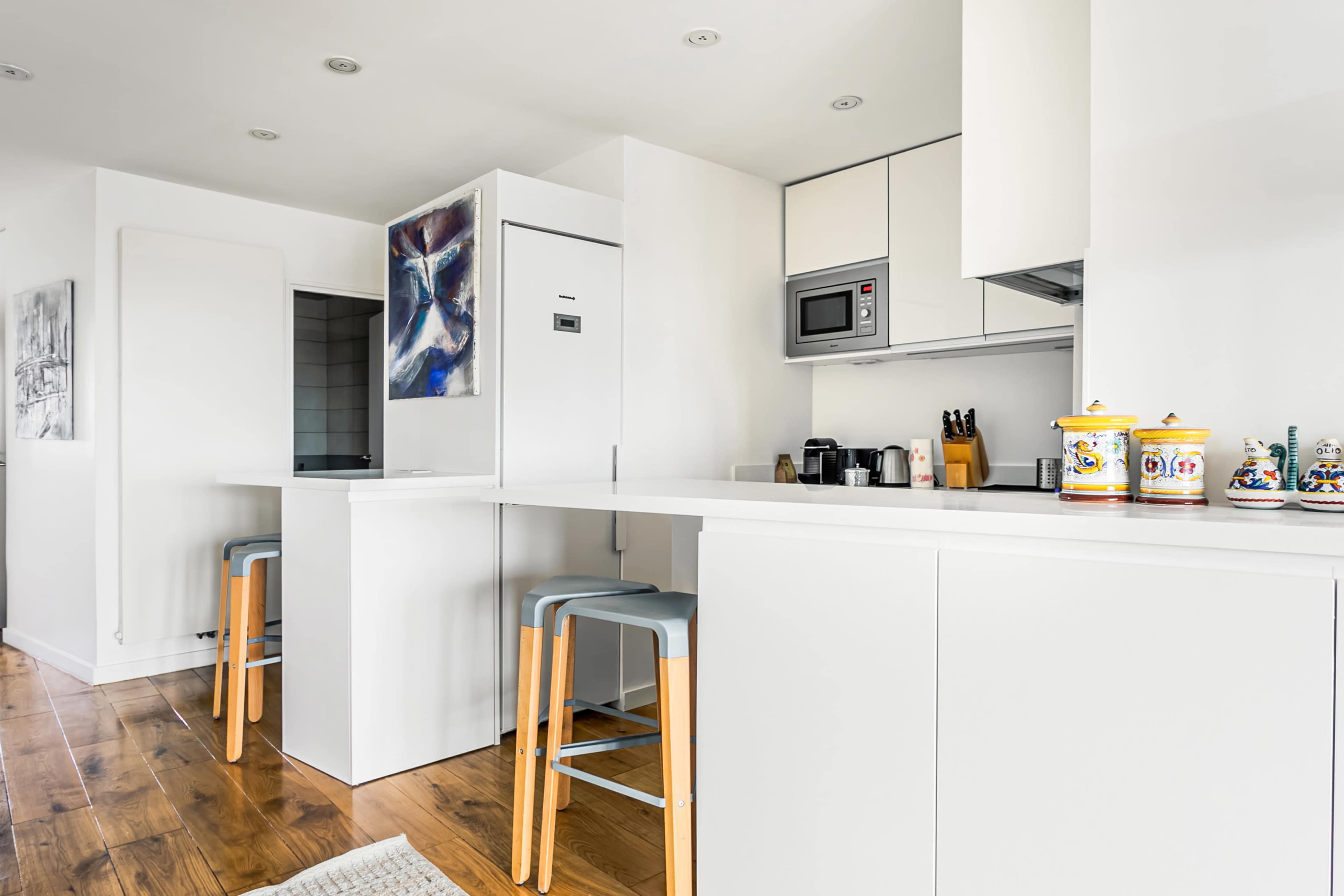 A modern kitchen with white cabinetry, a counter with stools, and a wall-mounted microwave.