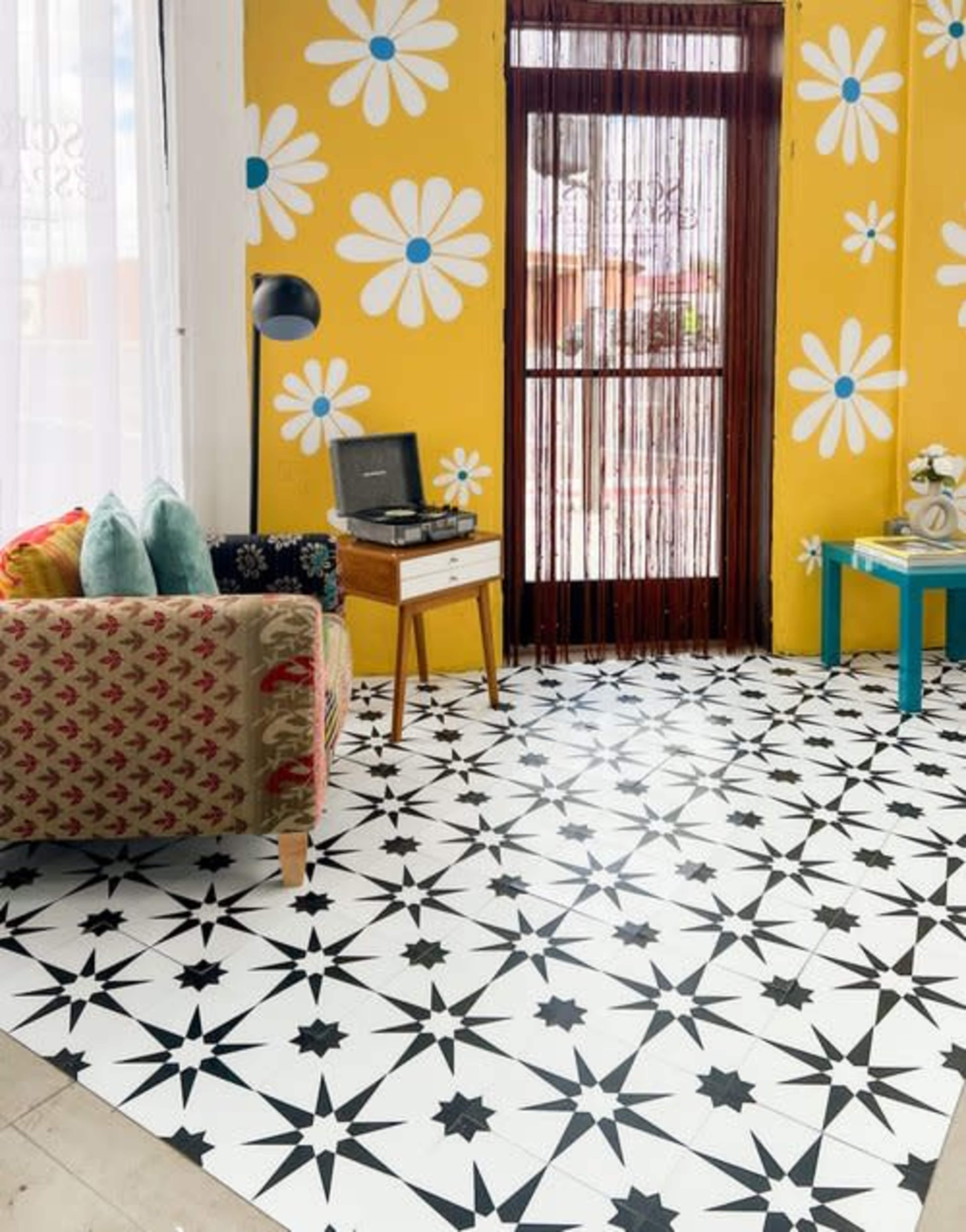 A bright, patterned room with a yellow wall decorated with daisies, a patterned couch, and a wooden table displaying a vintage record player.