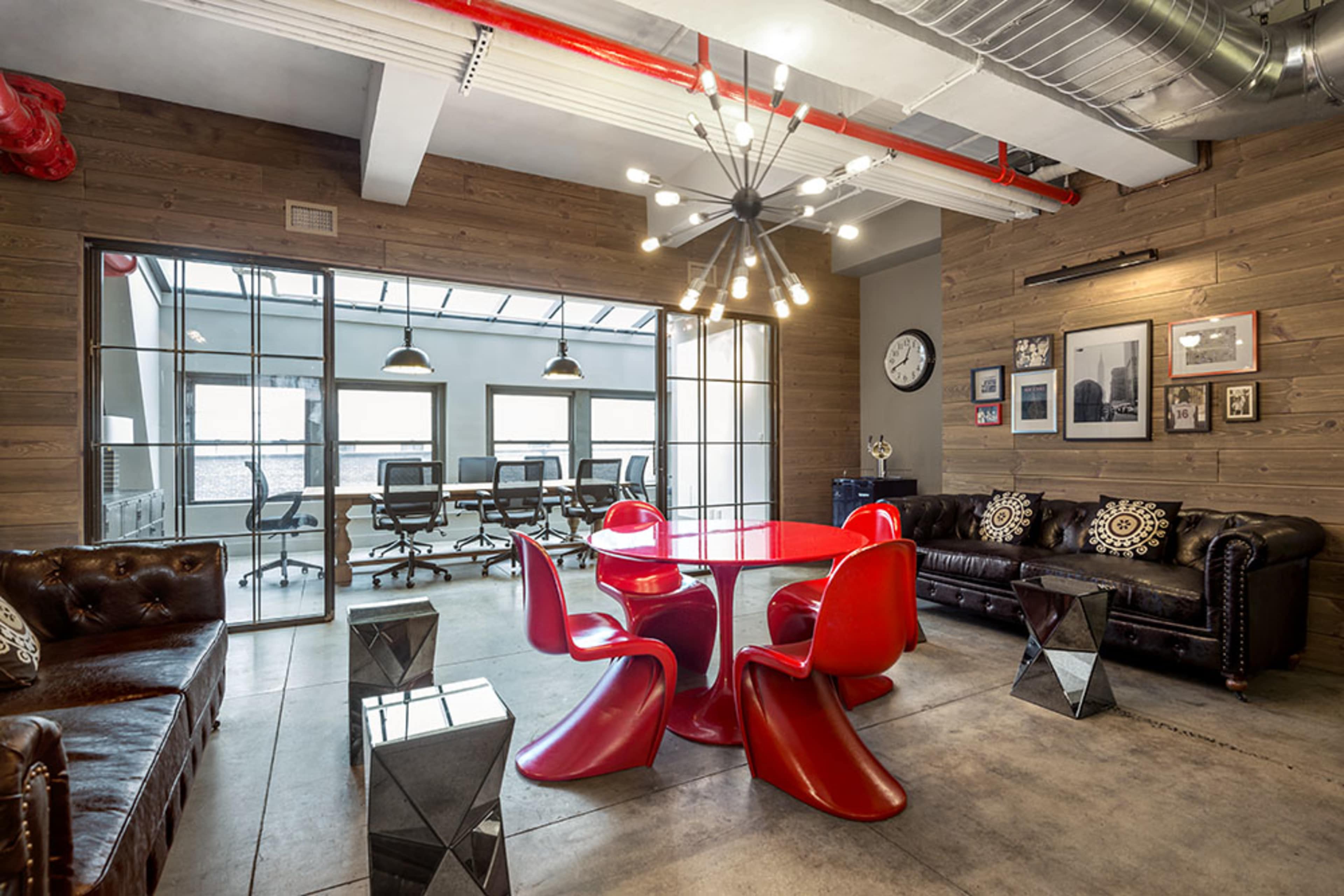 A modern office space featuring red furniture, leather sofas, and a glass meeting room in the background.