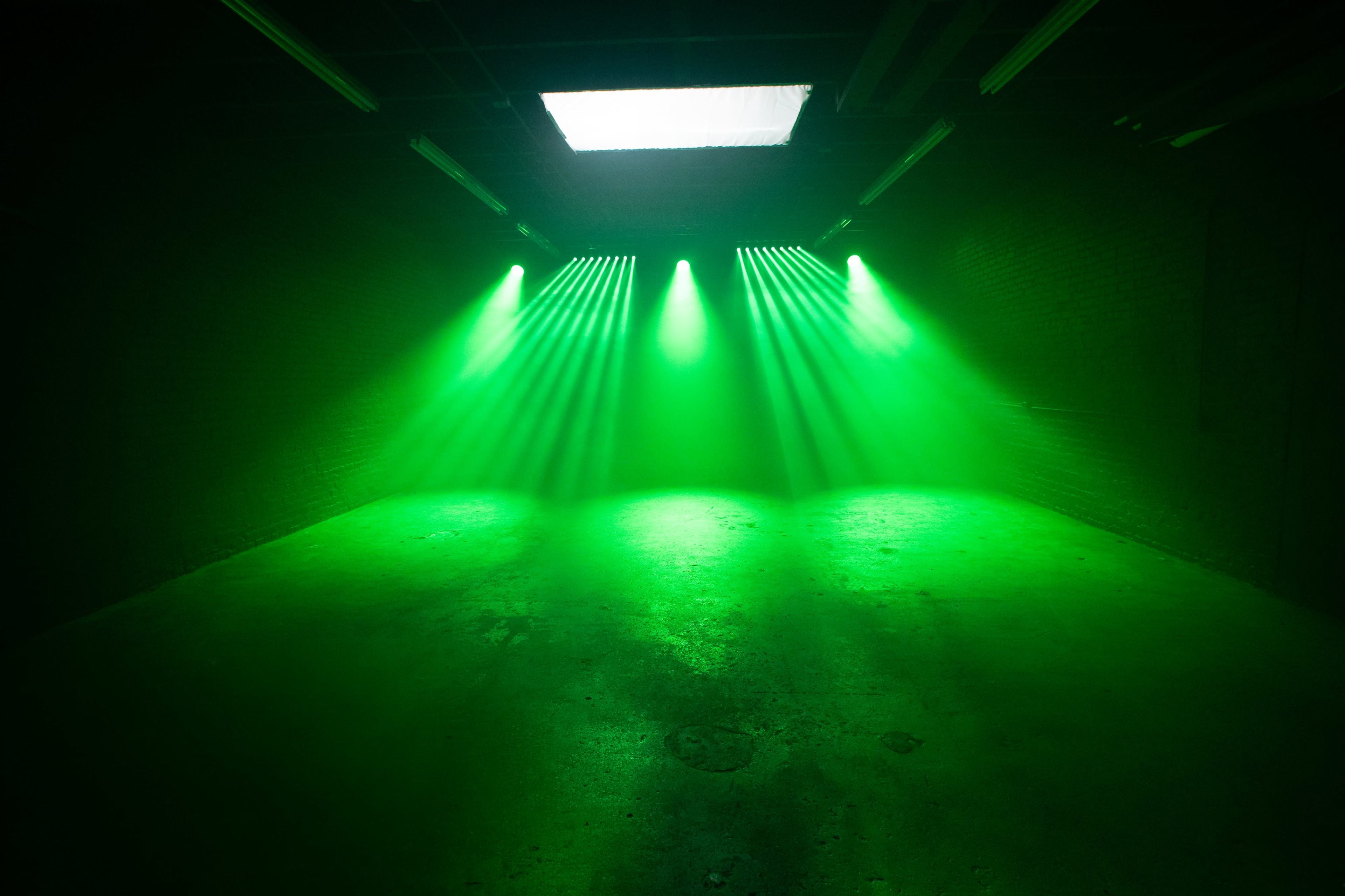 The image shows a dimly lit room with green stage lights casting beams across the concrete floor.