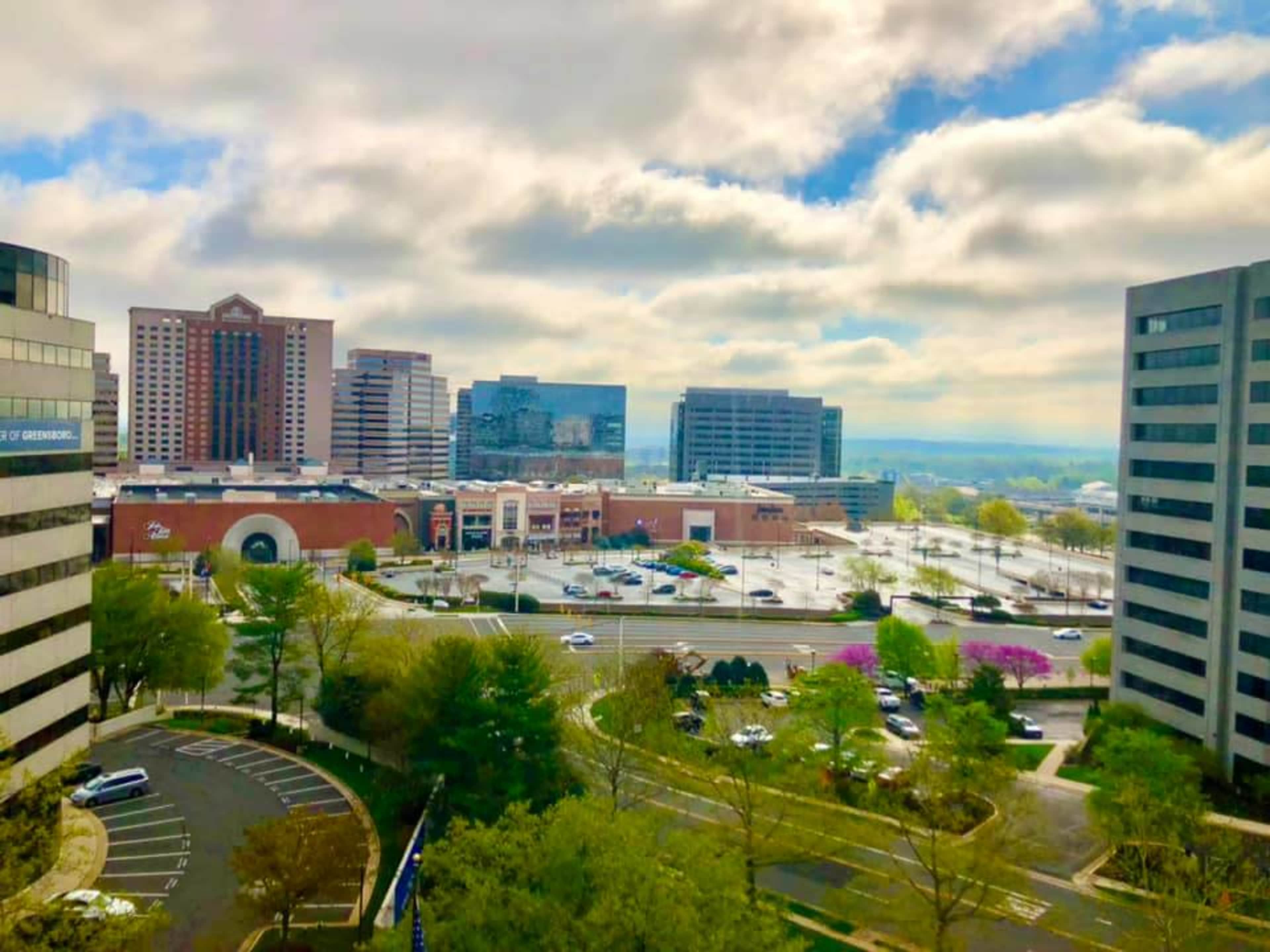 A city skyline with office buildings, a shopping plaza, and a partially cloudy sky.