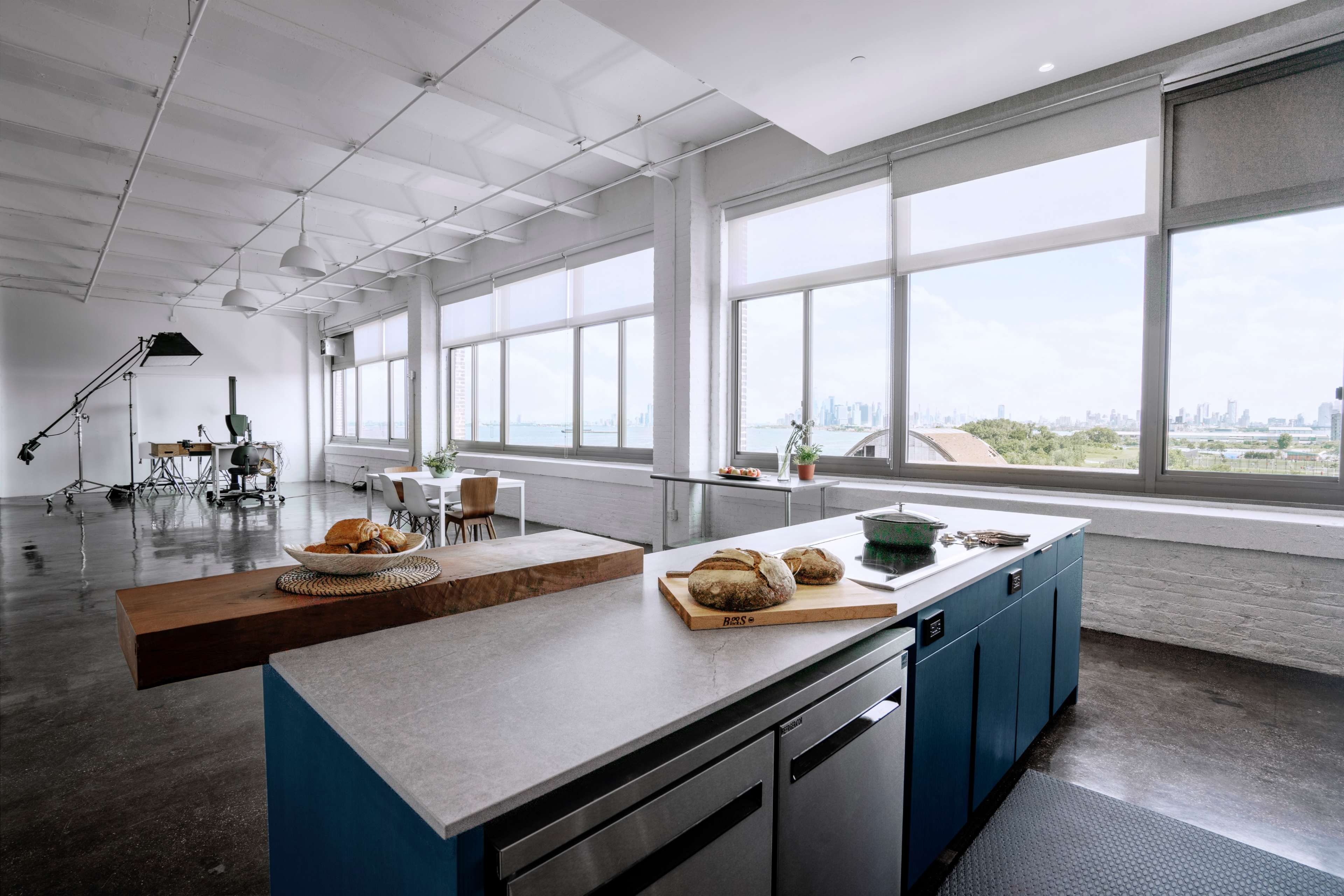A bright, modern kitchen features a wooden island with baked goods and large windows overlooking a city skyline.