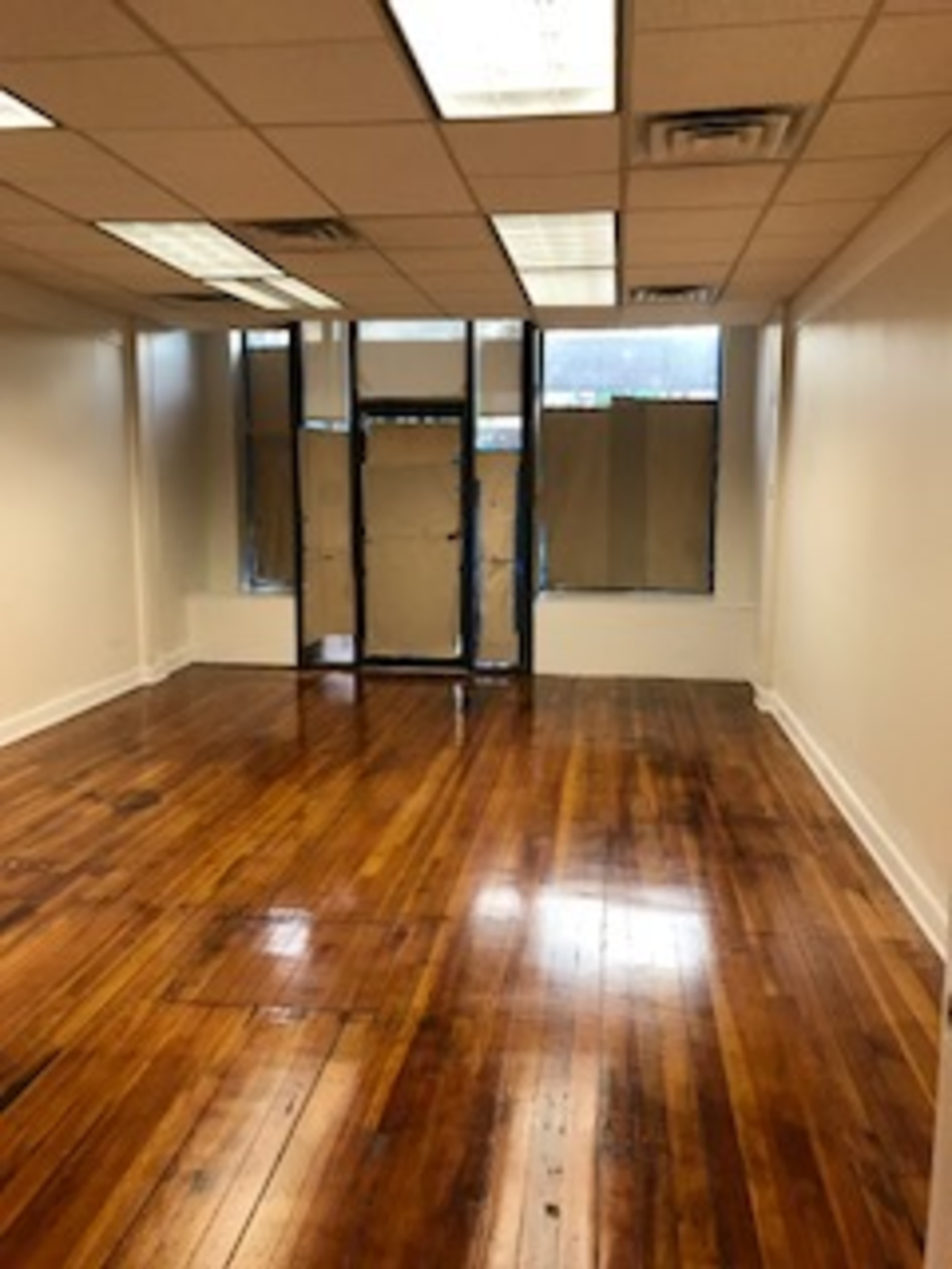 The image shows an empty room with hardwood floors, white walls, and large windows covered with brown paper.