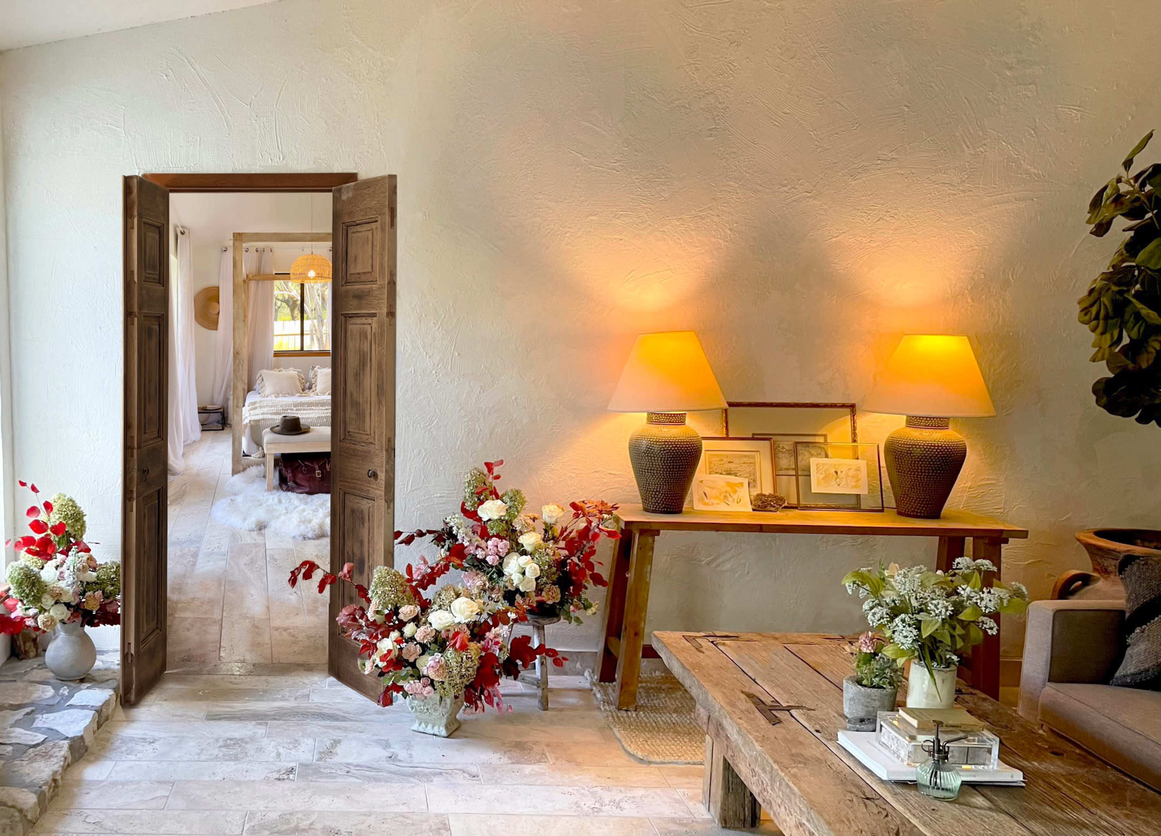 A welcoming entrance features a set of open double doors leading to a cozy room, with a table adorned with flowers and two lamps casting a warm glow.