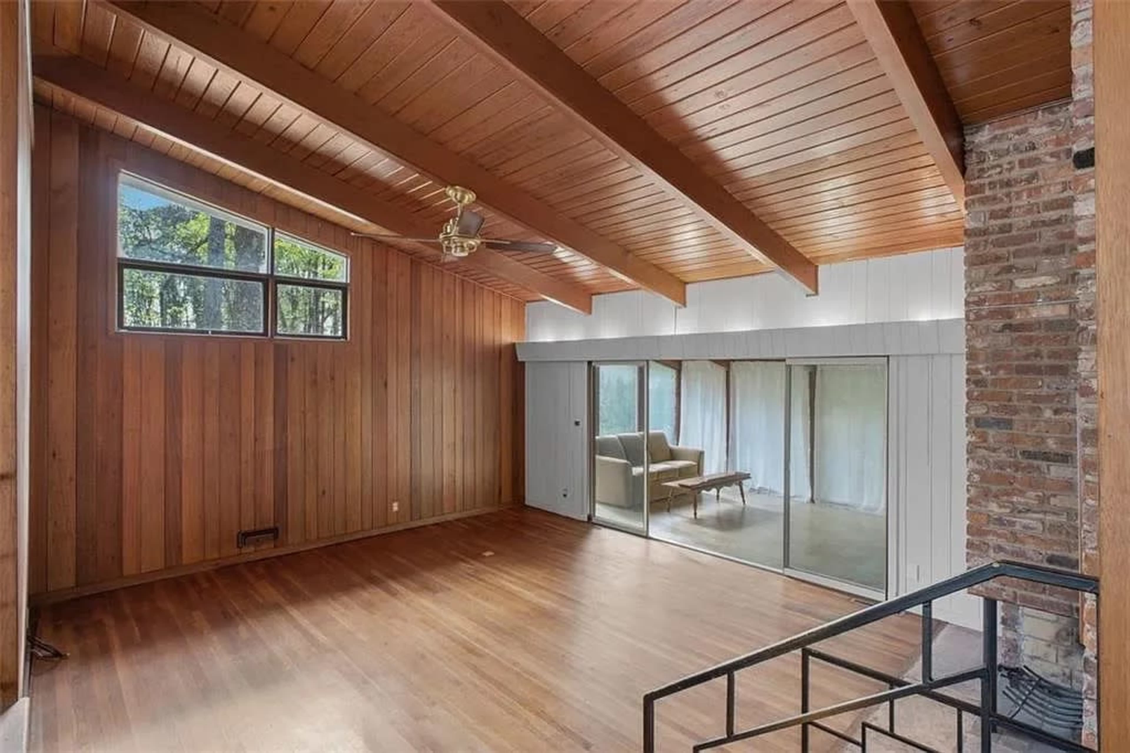 The room features wooden paneling and ceiling beams, with large glass doors opening to outside and a small staircase leading to another area.