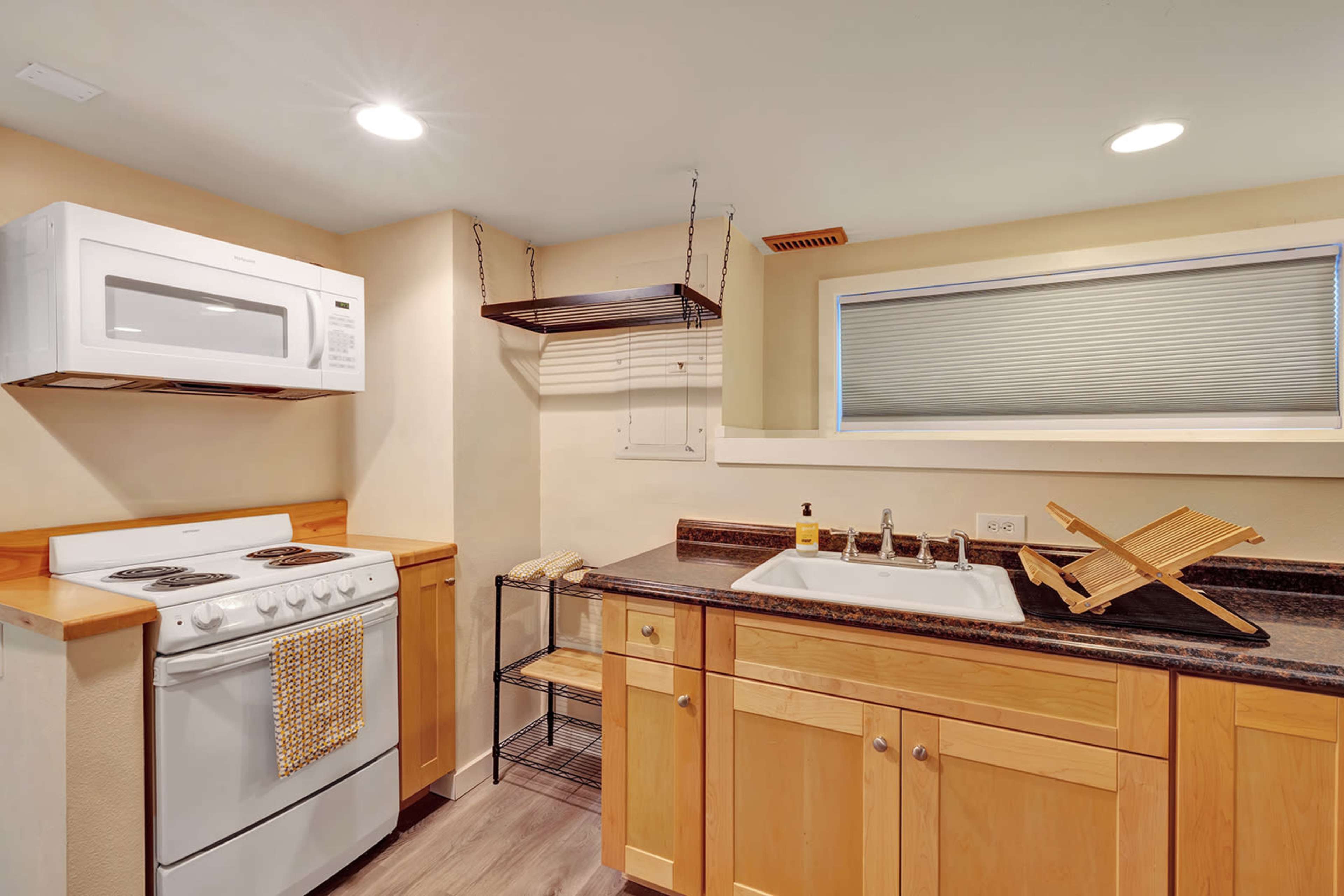 The image shows a compact kitchen featuring a stove, microwave, sink, and wooden cabinets.