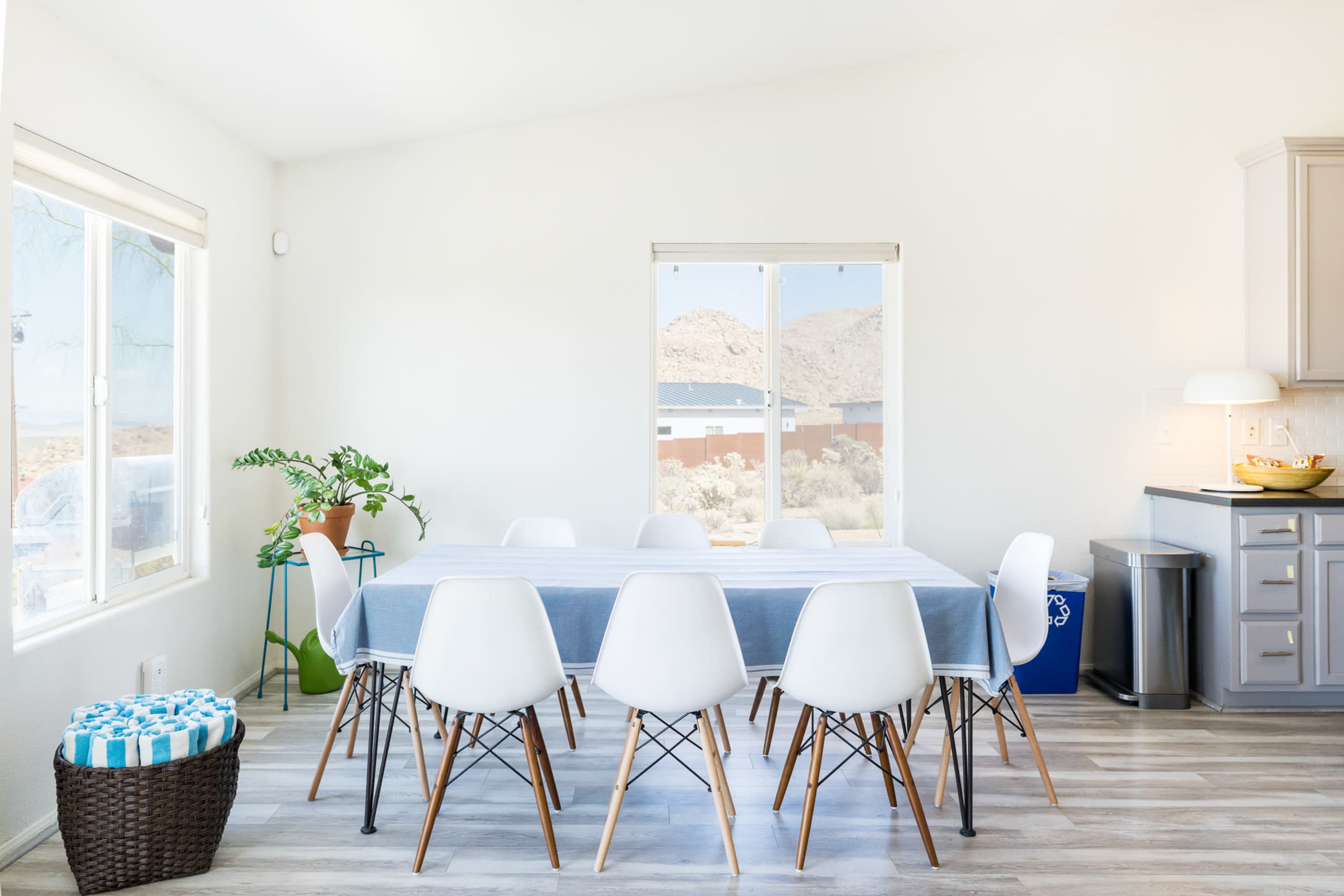A bright and airy dining area features a large white table surrounded by modern chairs, with a window offering a view of the outdoors.