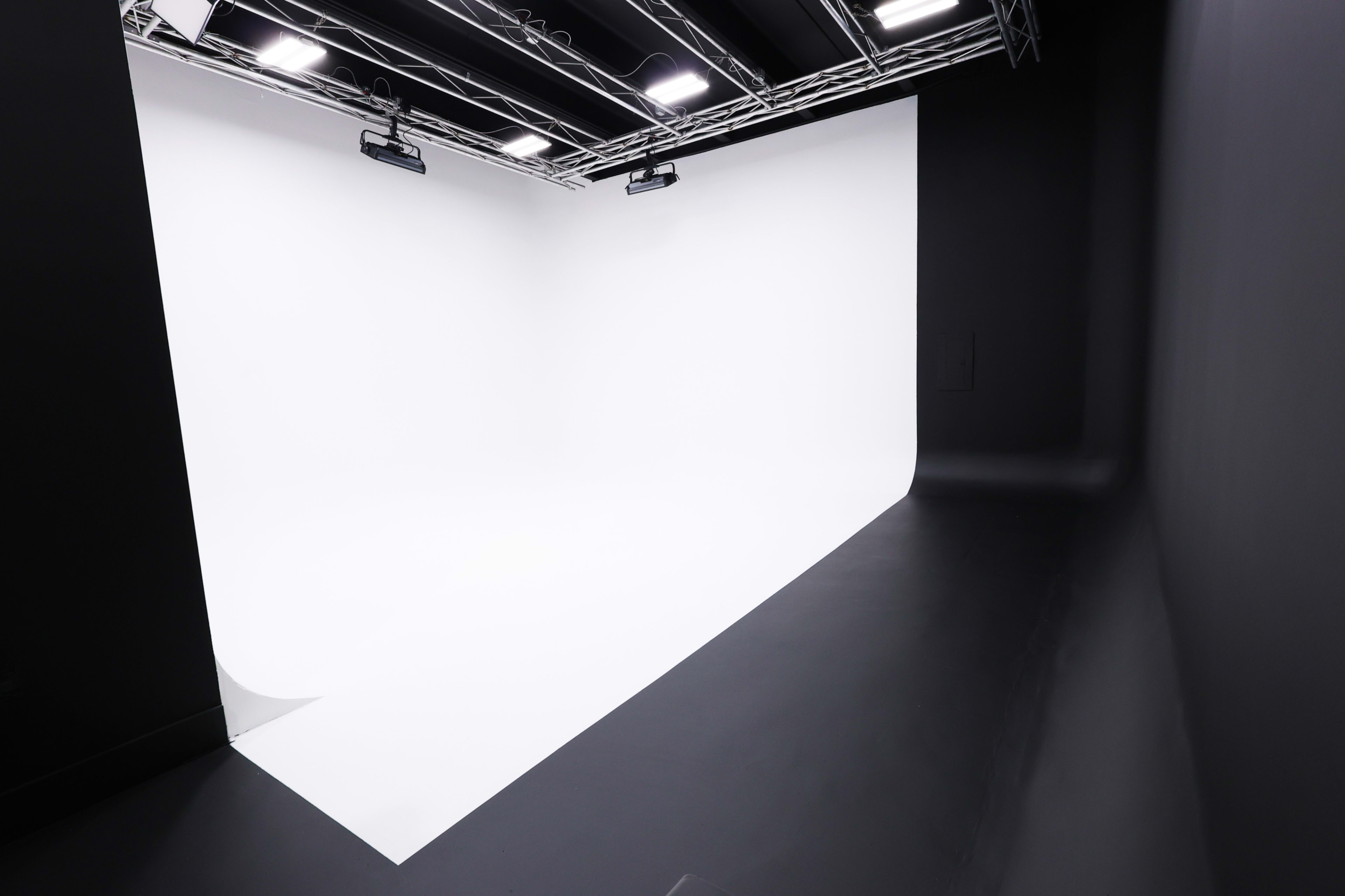 A photography studio features a seamless white backdrop with a curved transition and black walls.