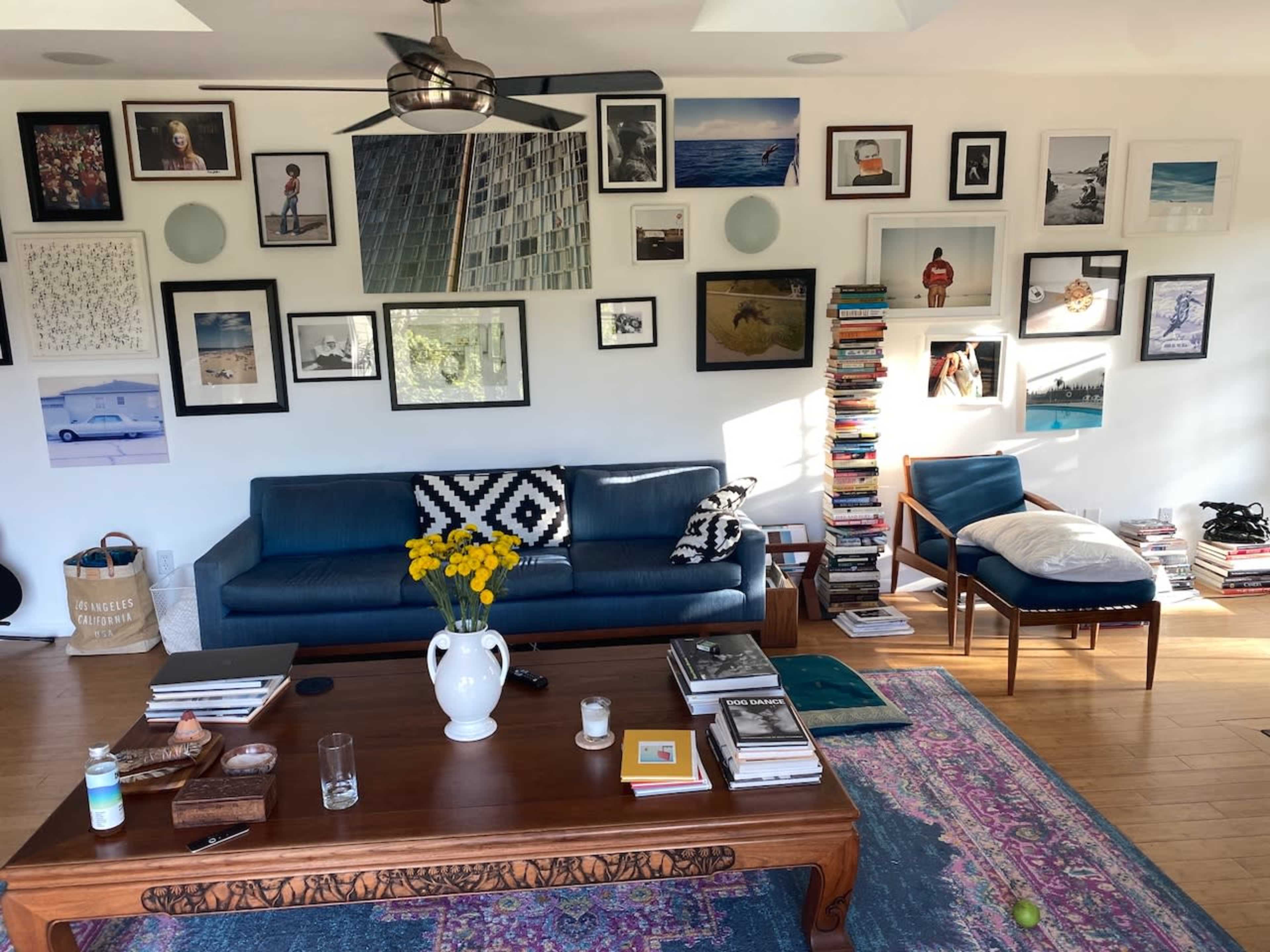 A cozy living room features a blue sofa, a wooden coffee table with various items, and walls adorned with a collection of framed artwork and photographs.