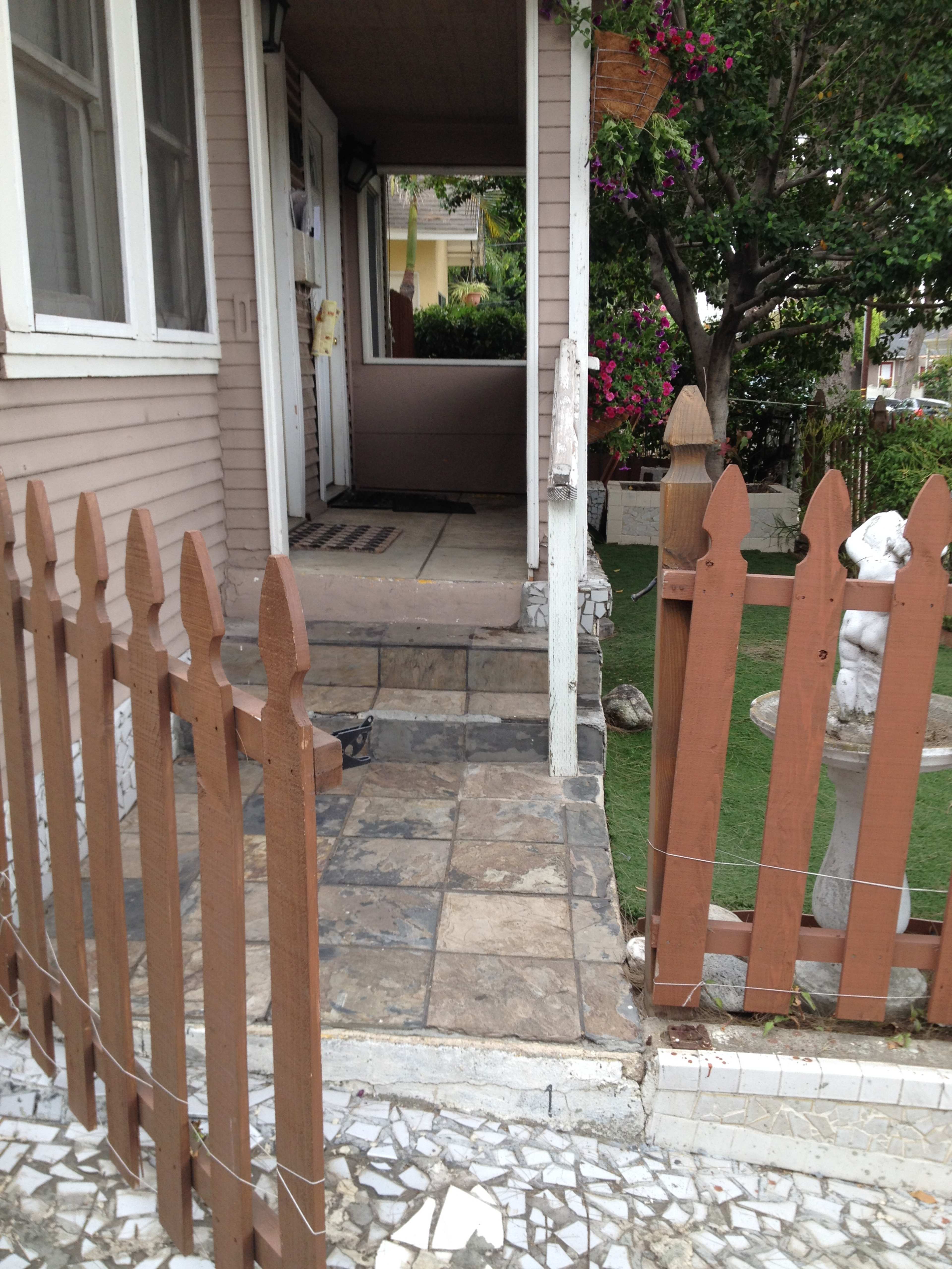 A small porch with stone steps leading up to an entrance, surrounded by a brown wooden fence and a garden area.