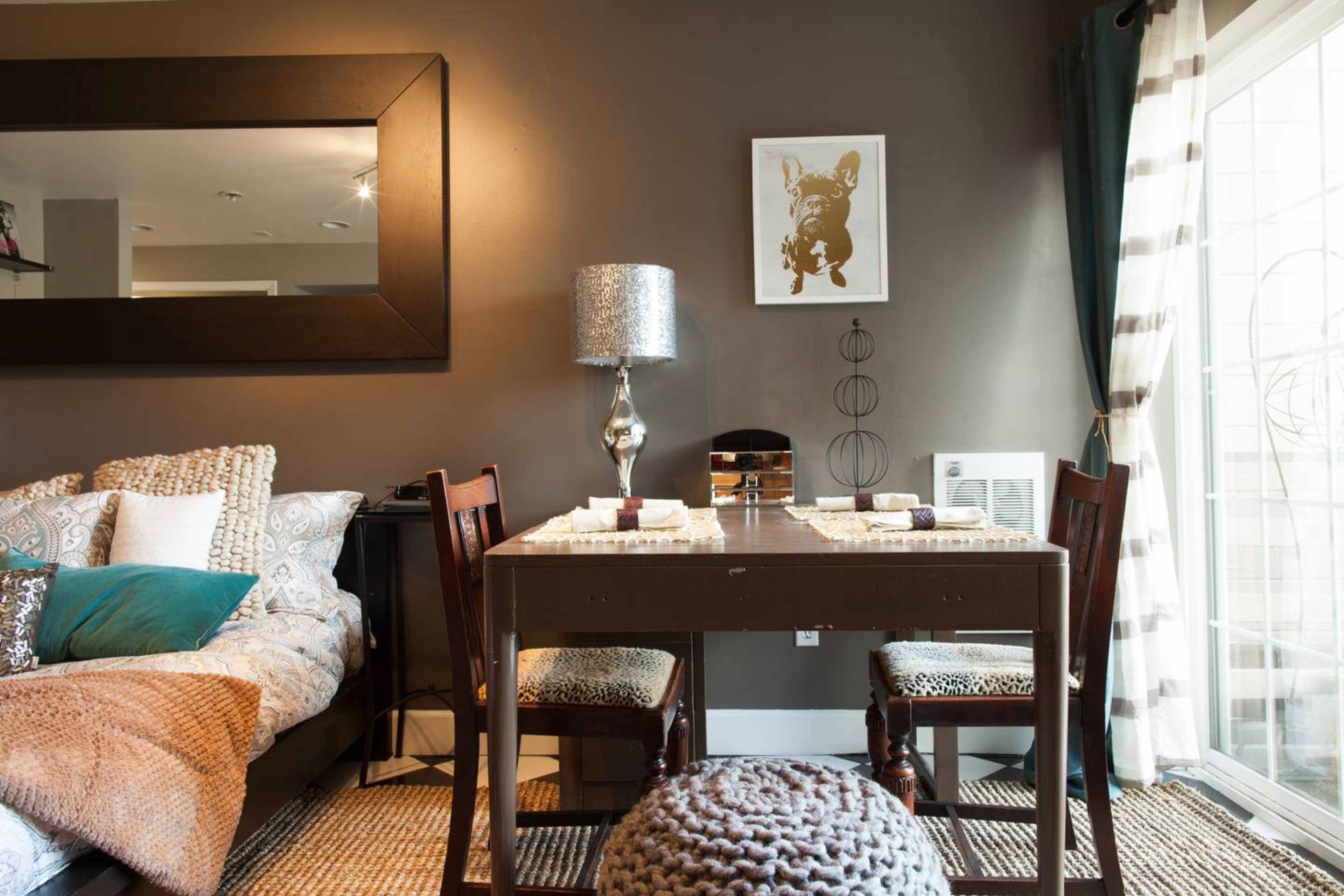 A small dining area with a table set for two, surrounded by a cozy couch and a decorative wall mirror on a dark wall.