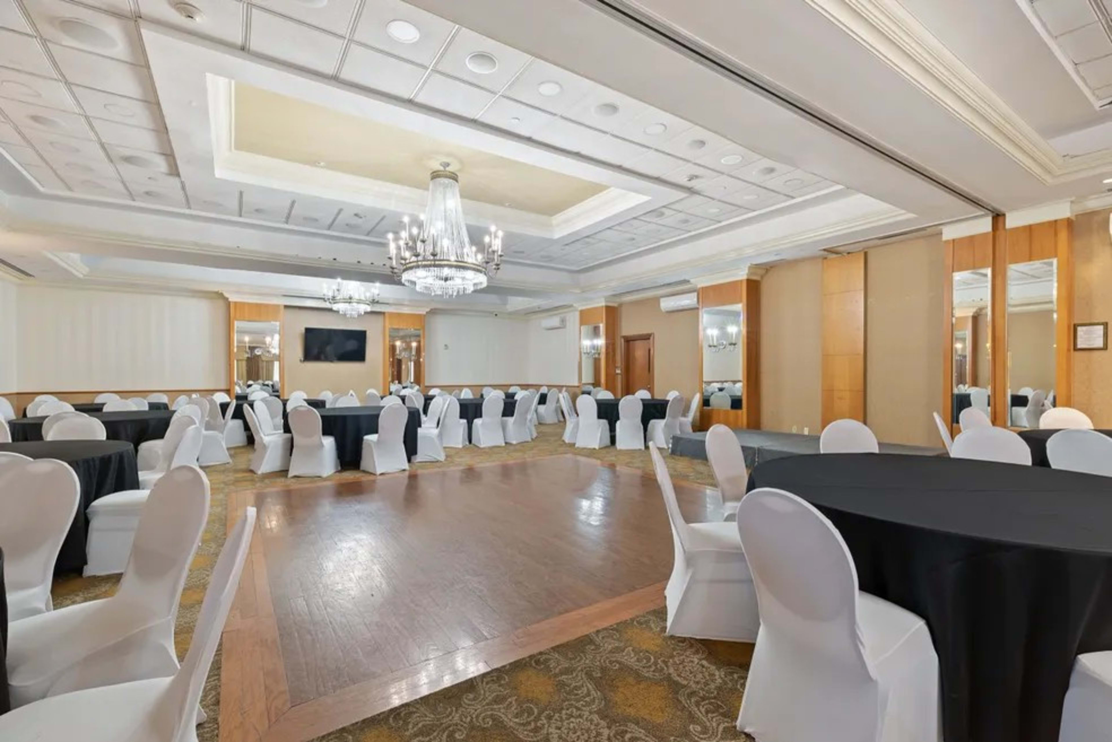 A banquet hall with round tables covered in black and white tablecloths, surrounded by white chairs and illuminated by a chandelier.
