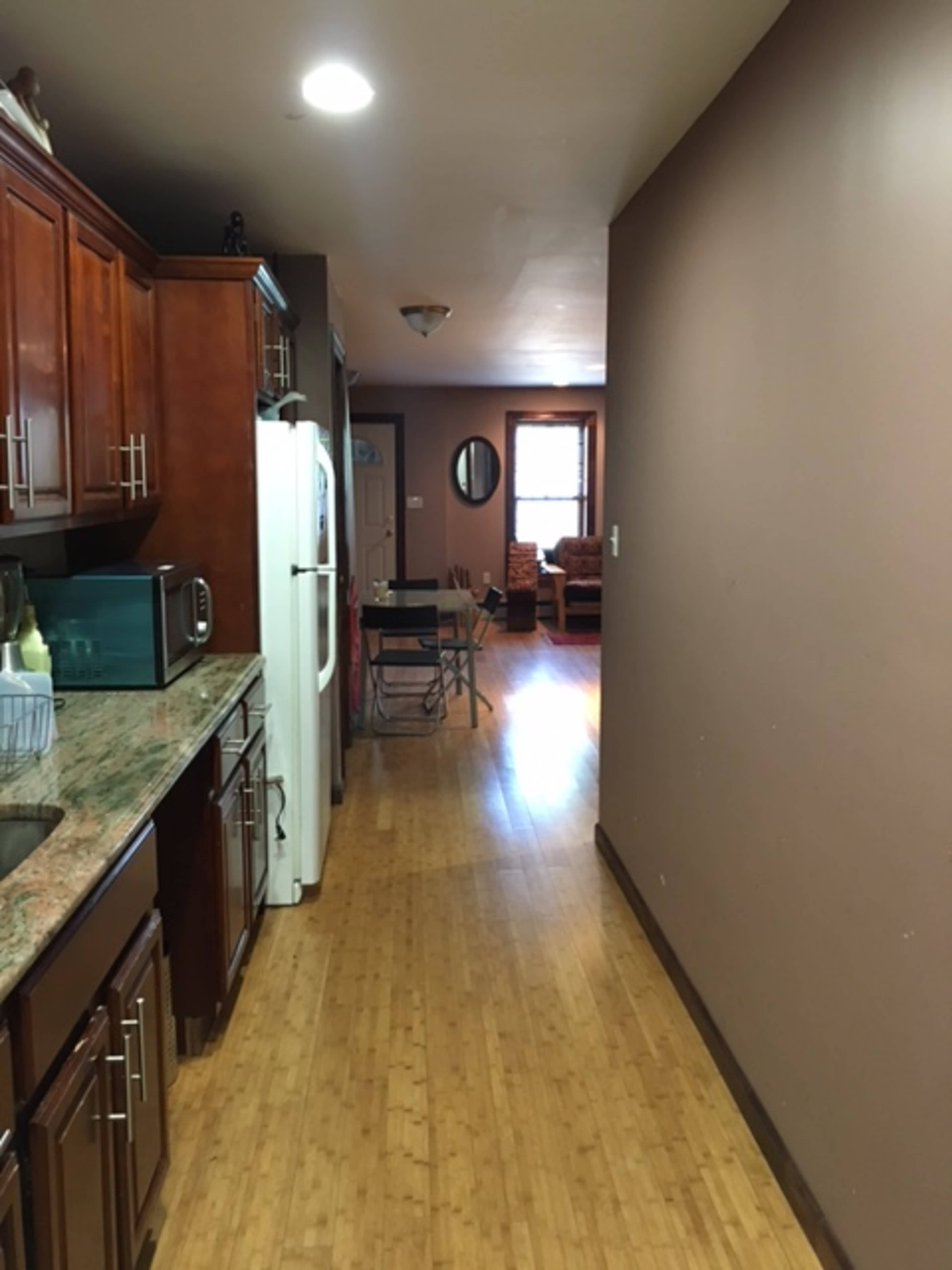 A hallway leading from a kitchen with wooden cabinets to a living area with seating at the far end.