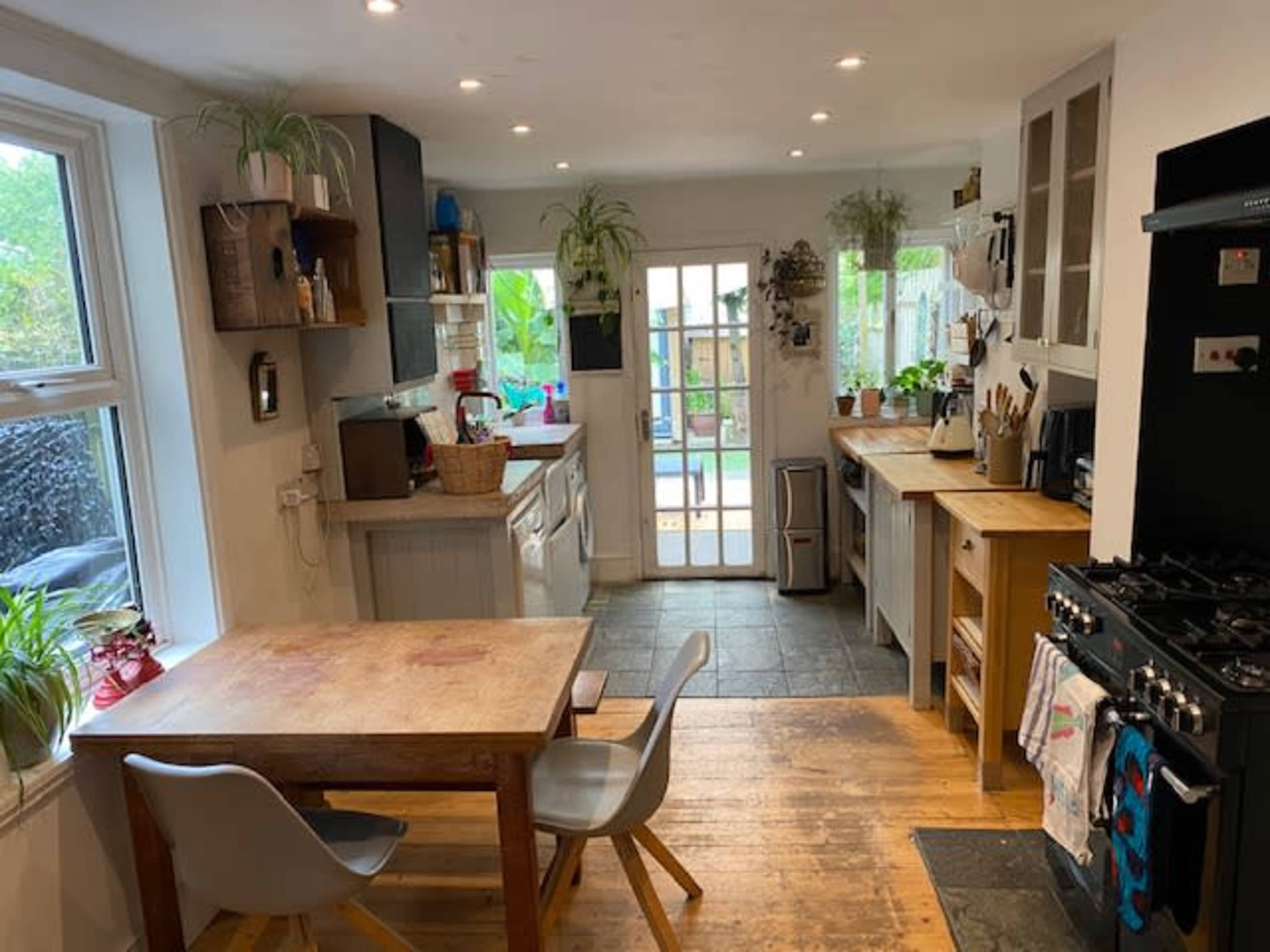The image shows a kitchen with a wooden table and chairs, appliances, and a door leading to an outdoor space.