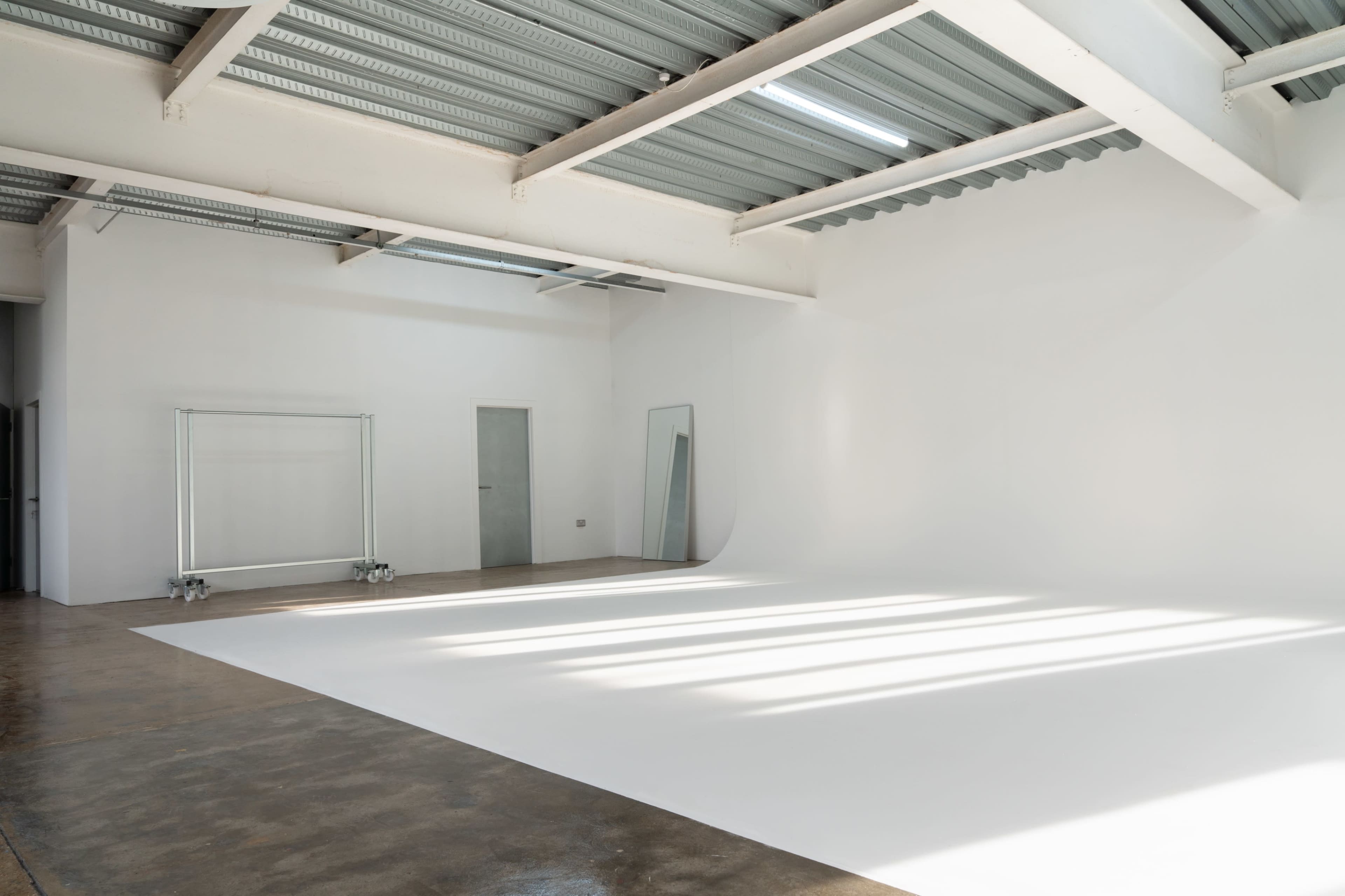 The image shows a spacious, white-walled studio with a smooth, white floor and shafts of light streaming through the ceiling.