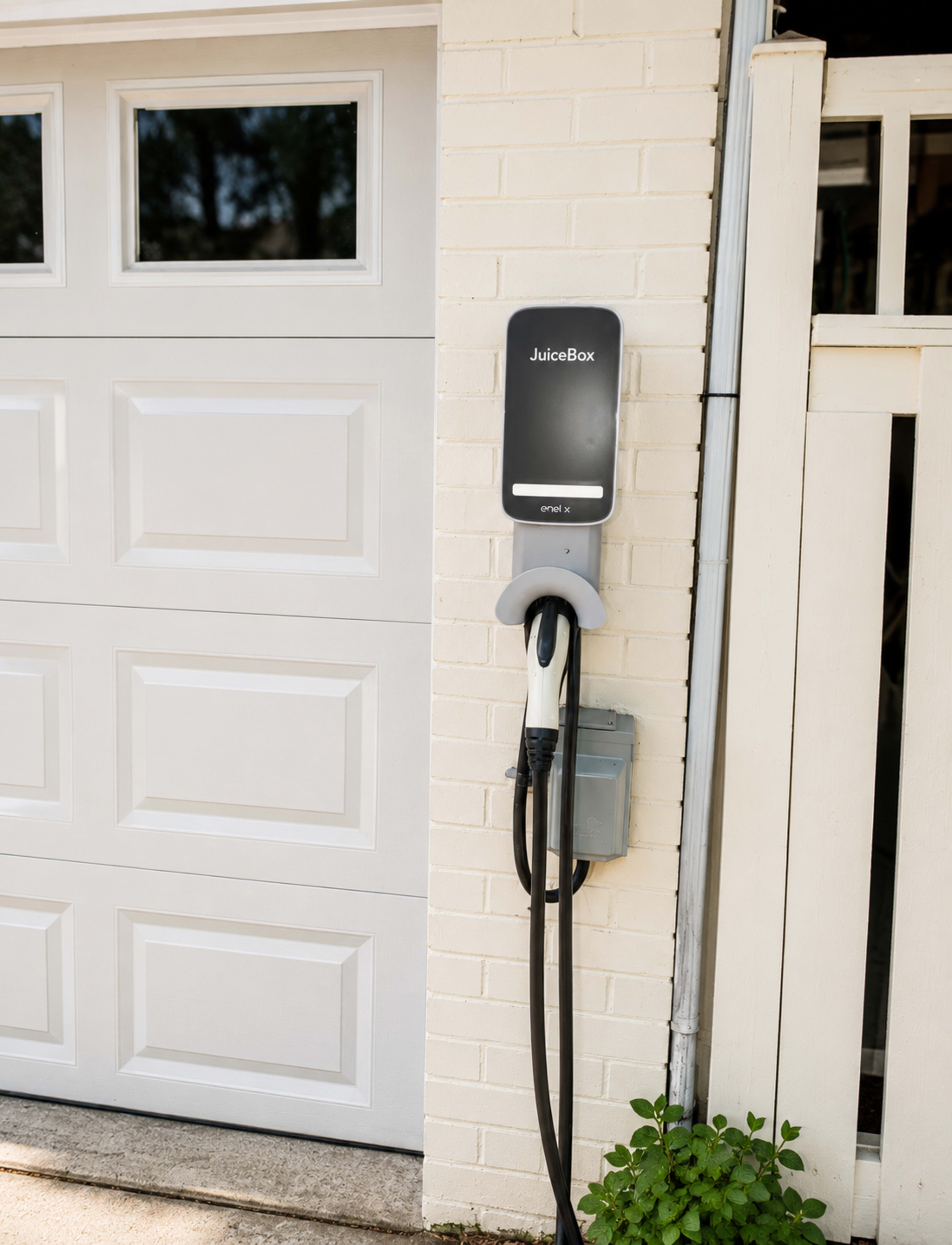 The image shows a JuiceBox EV charging station mounted on a white brick wall next to a garage door.