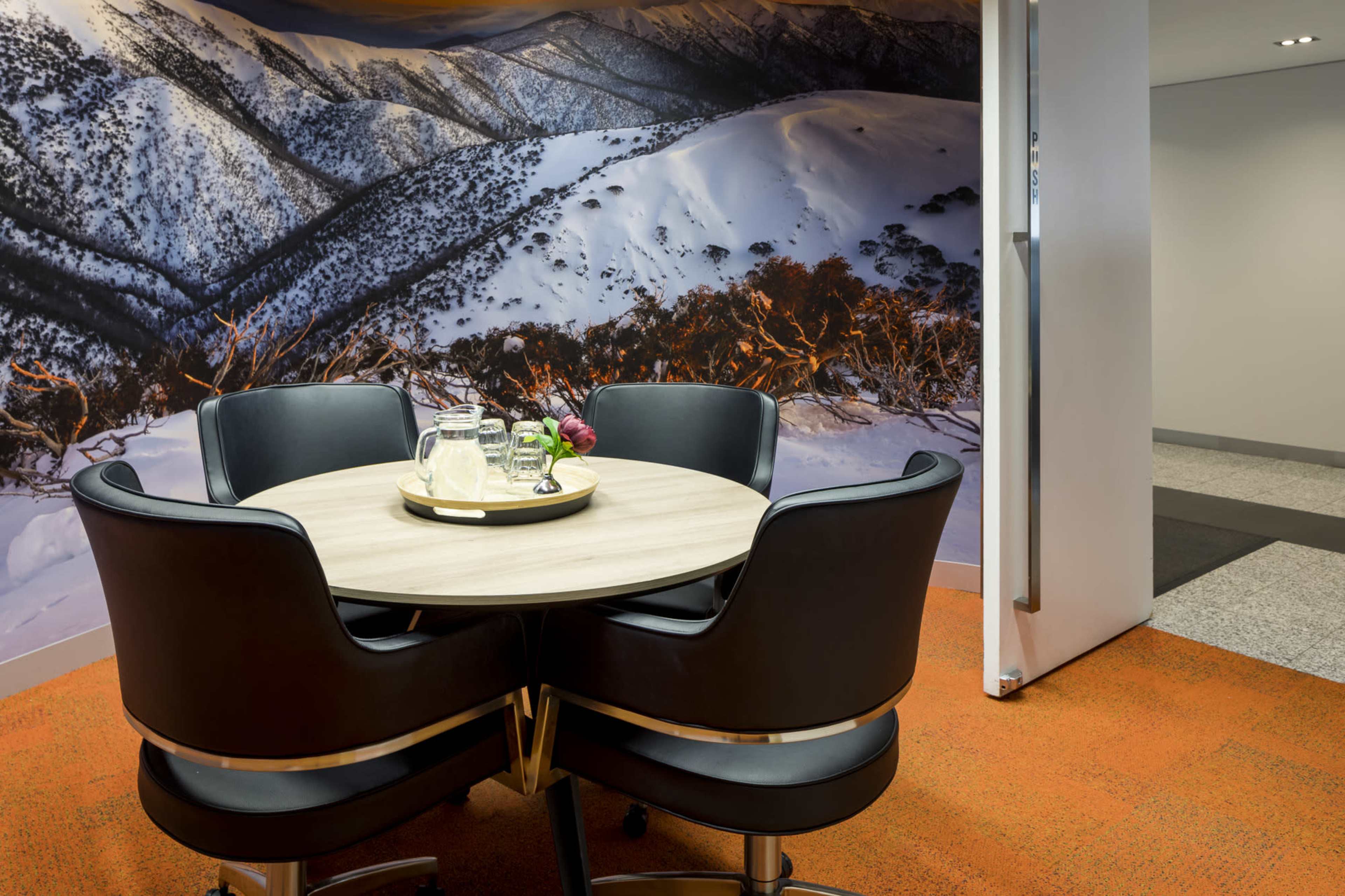 A round wooden table is set with a tray of refreshments in front of a wall mural depicting snow-covered mountains.