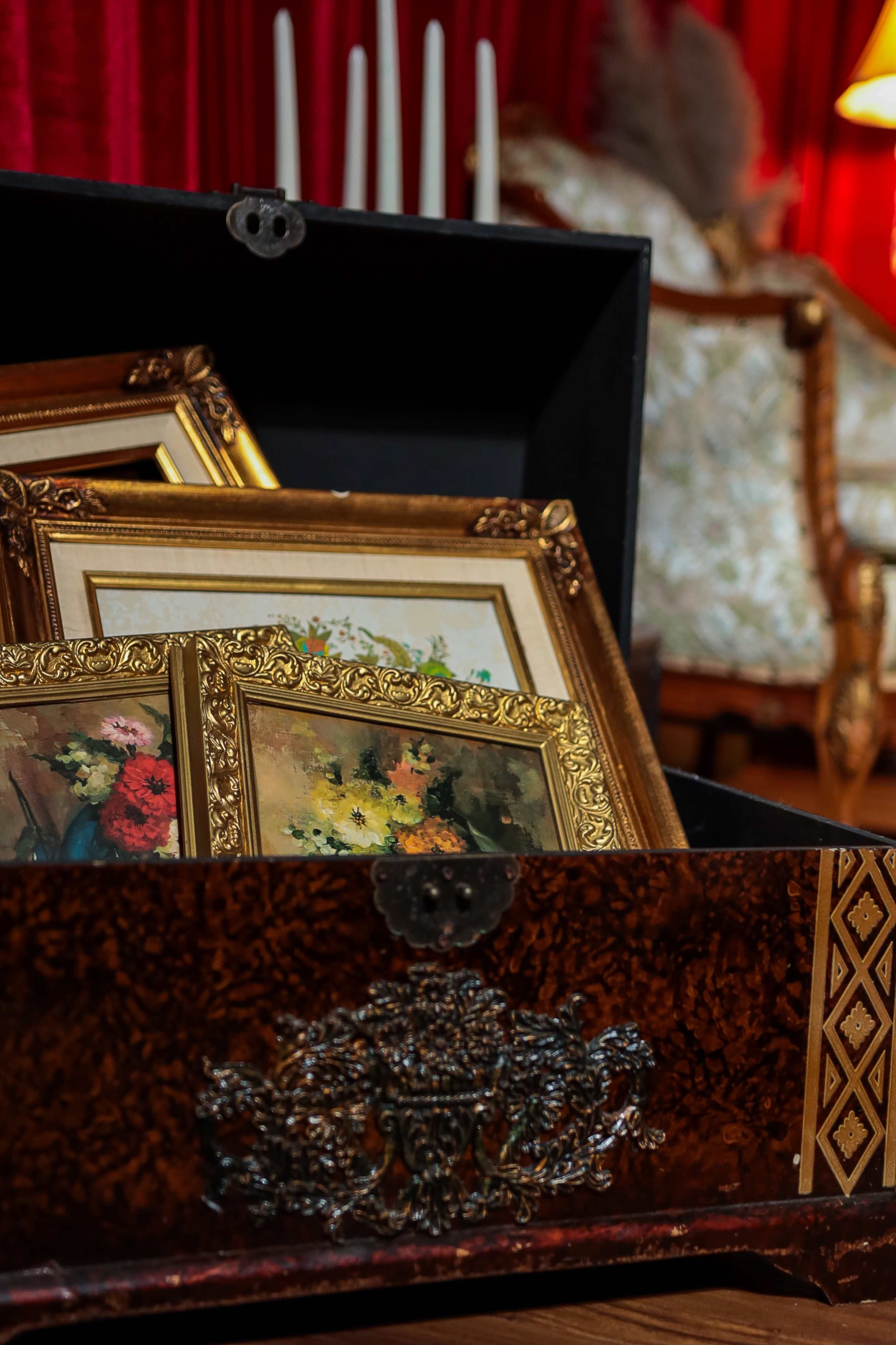 A decorative wooden box contains several framed paintings, while a couch and tall candles are visible in the background.