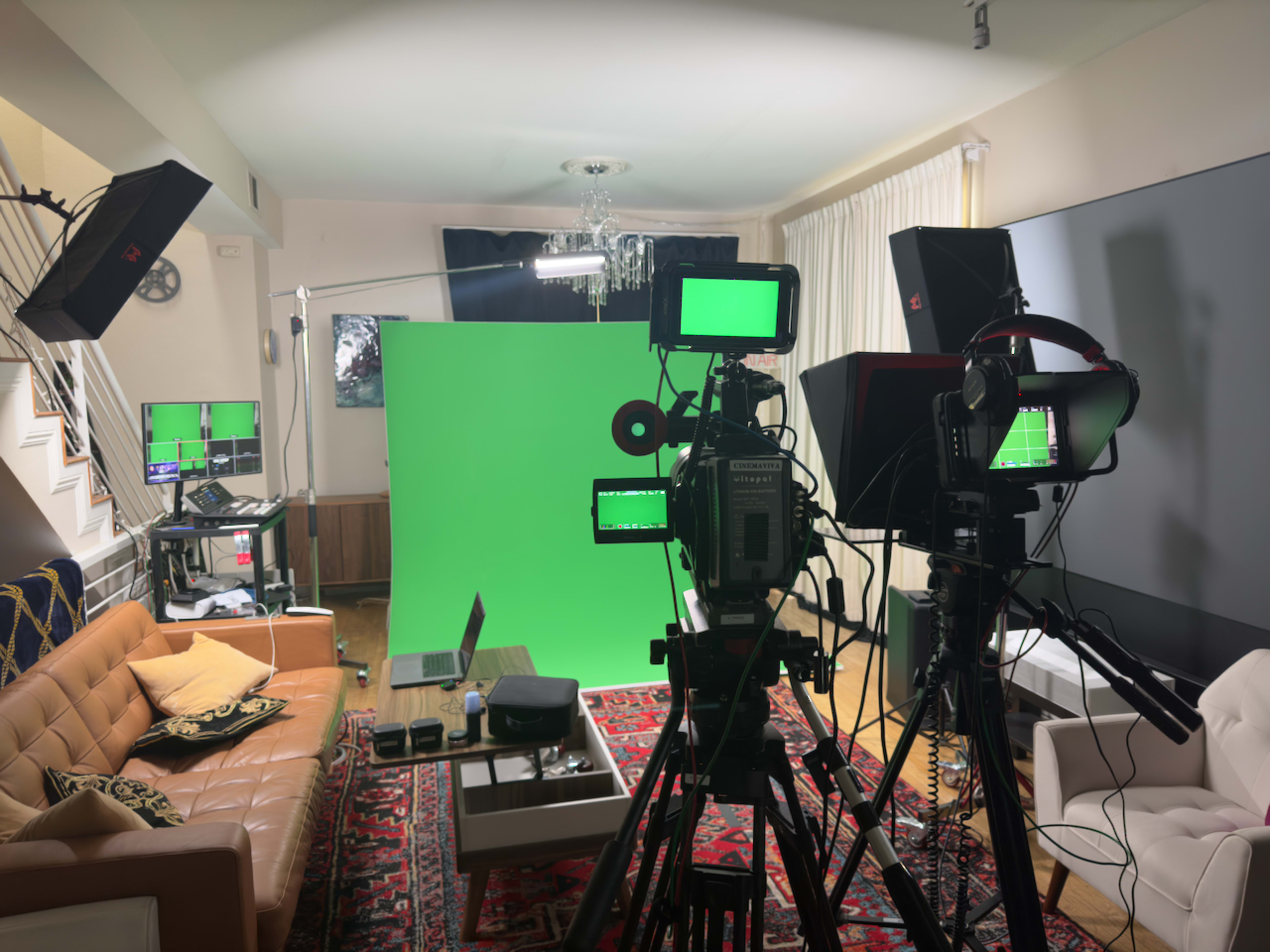 A studio setup features multiple cameras, lighting equipment, and a green screen, arranged in a well-furnished room.
