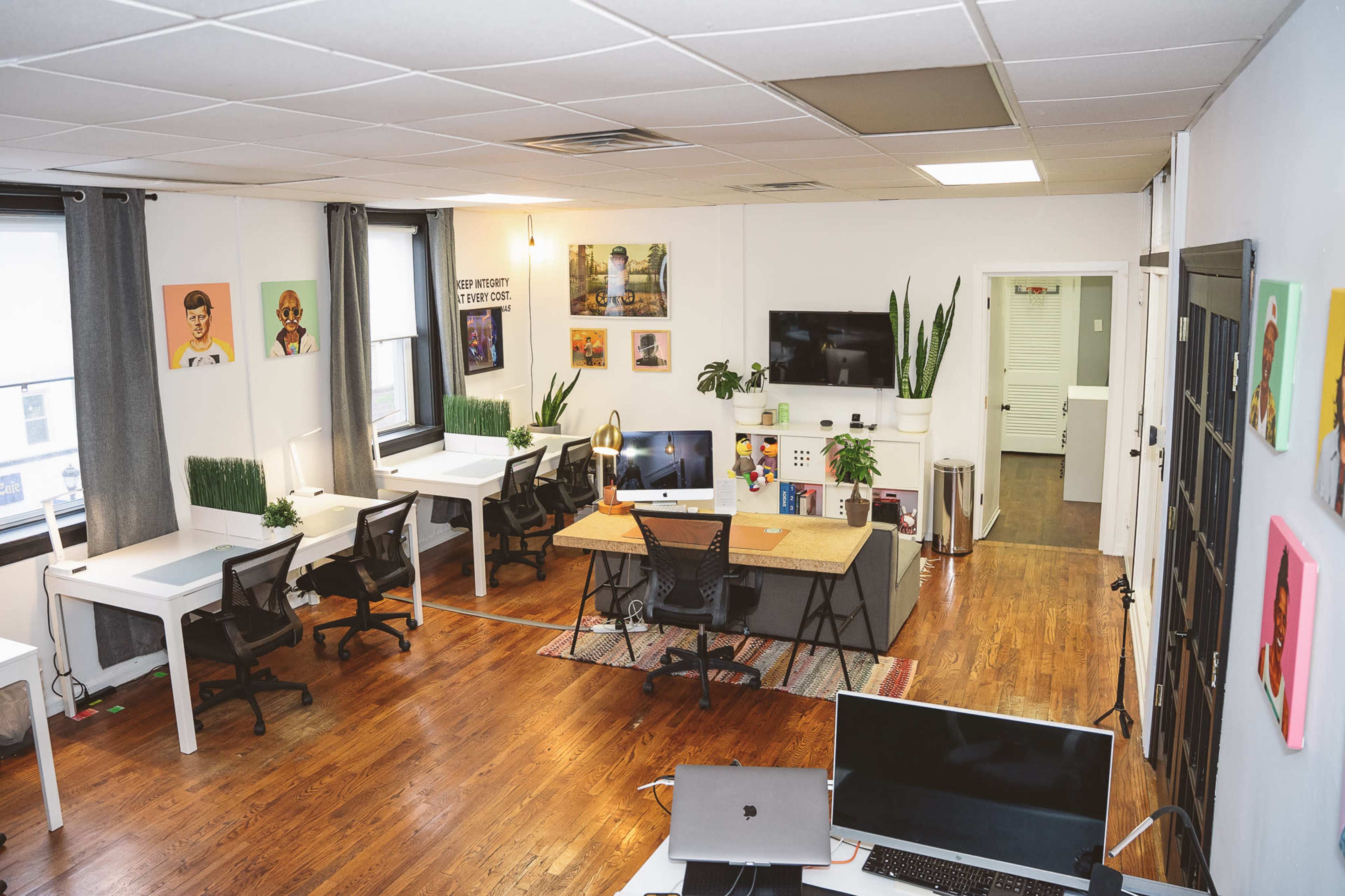 A modern office space with several desks, chairs, and wall decorations, featuring plants and a central work area with a large desk.