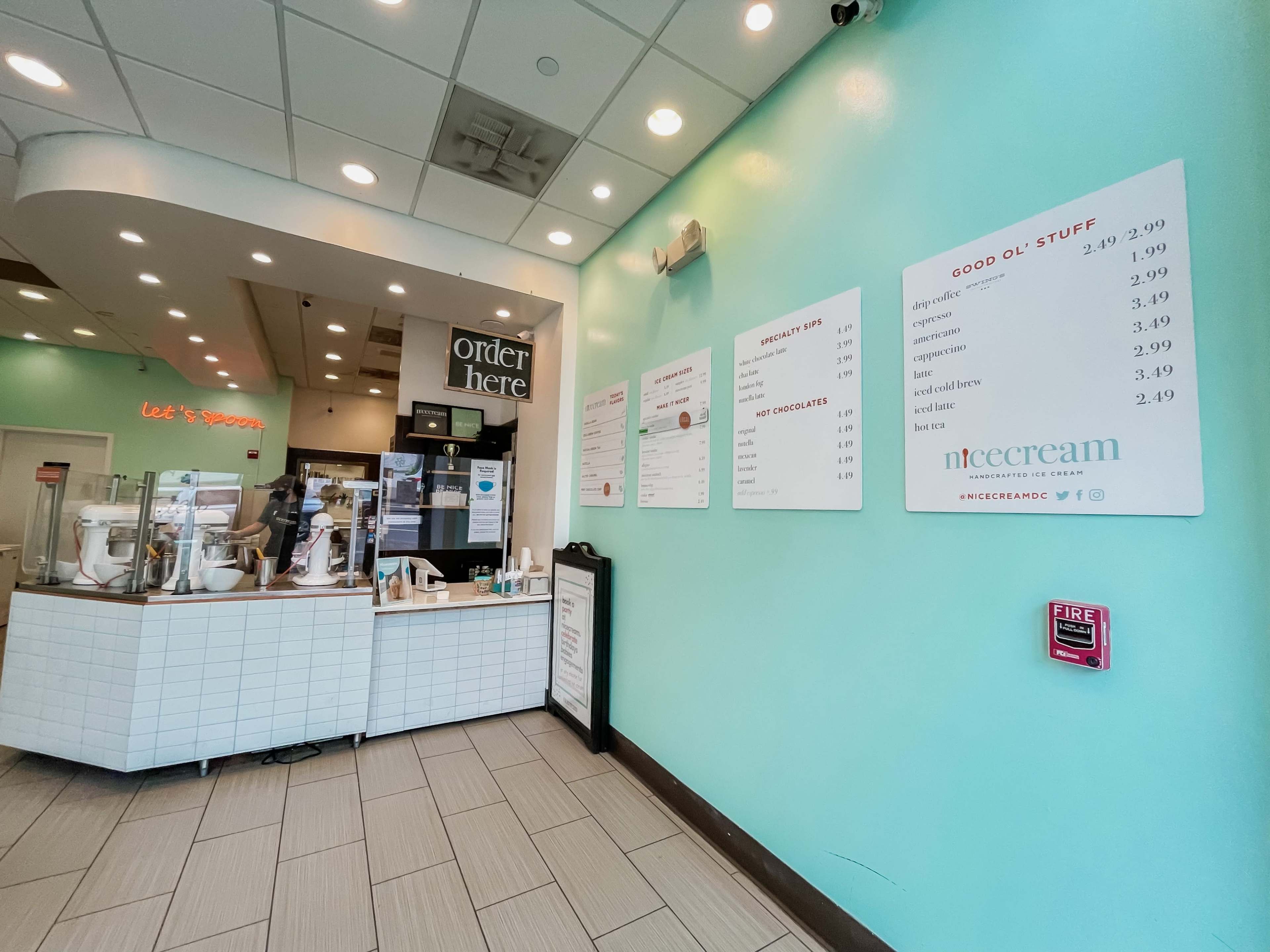 The image shows the interior of an ice cream shop with a counter displaying the menu and a brightly colored wall.