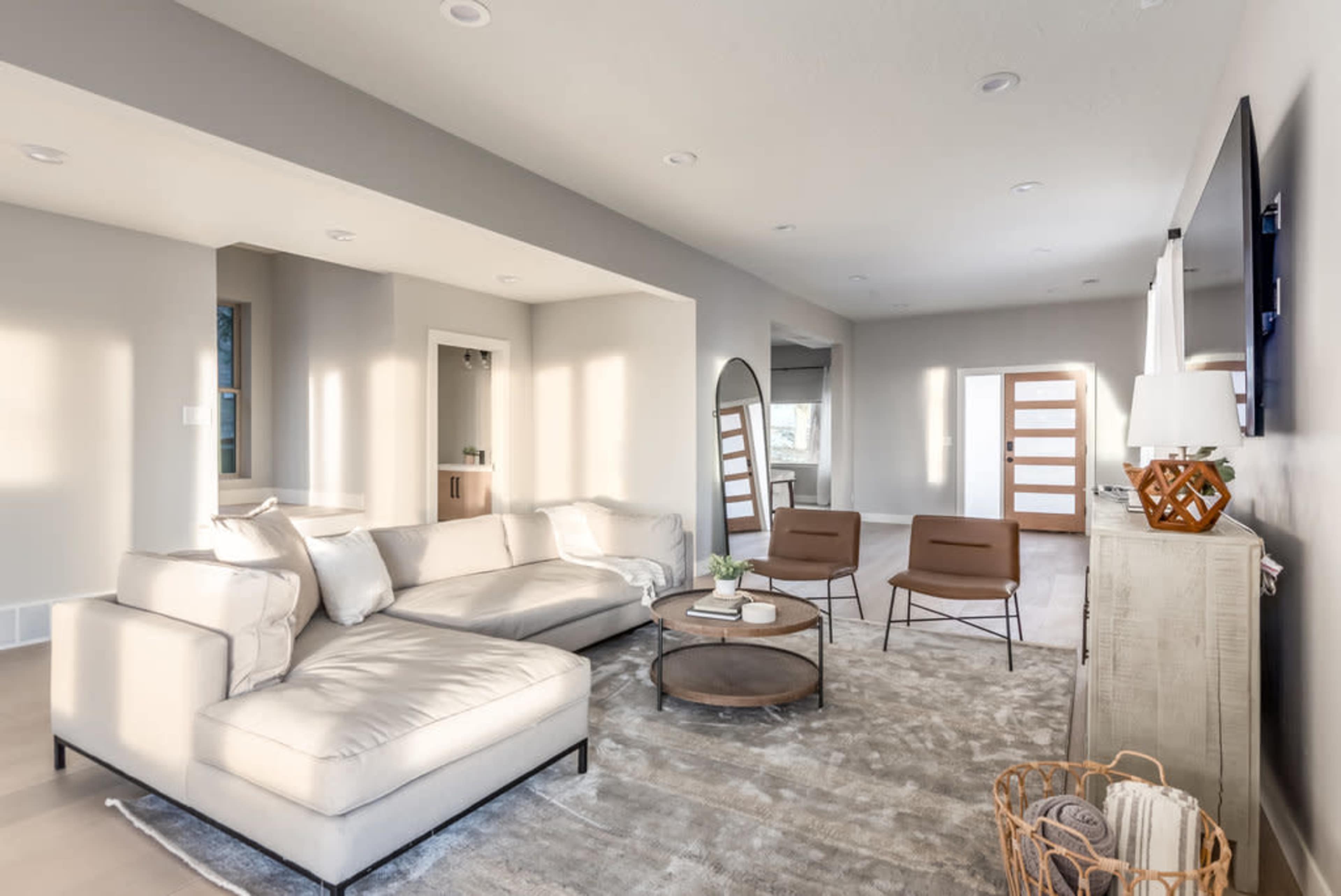 A modern living room with a sectional sofa, two armchairs, a round coffee table, and natural light coming through multiple windows.