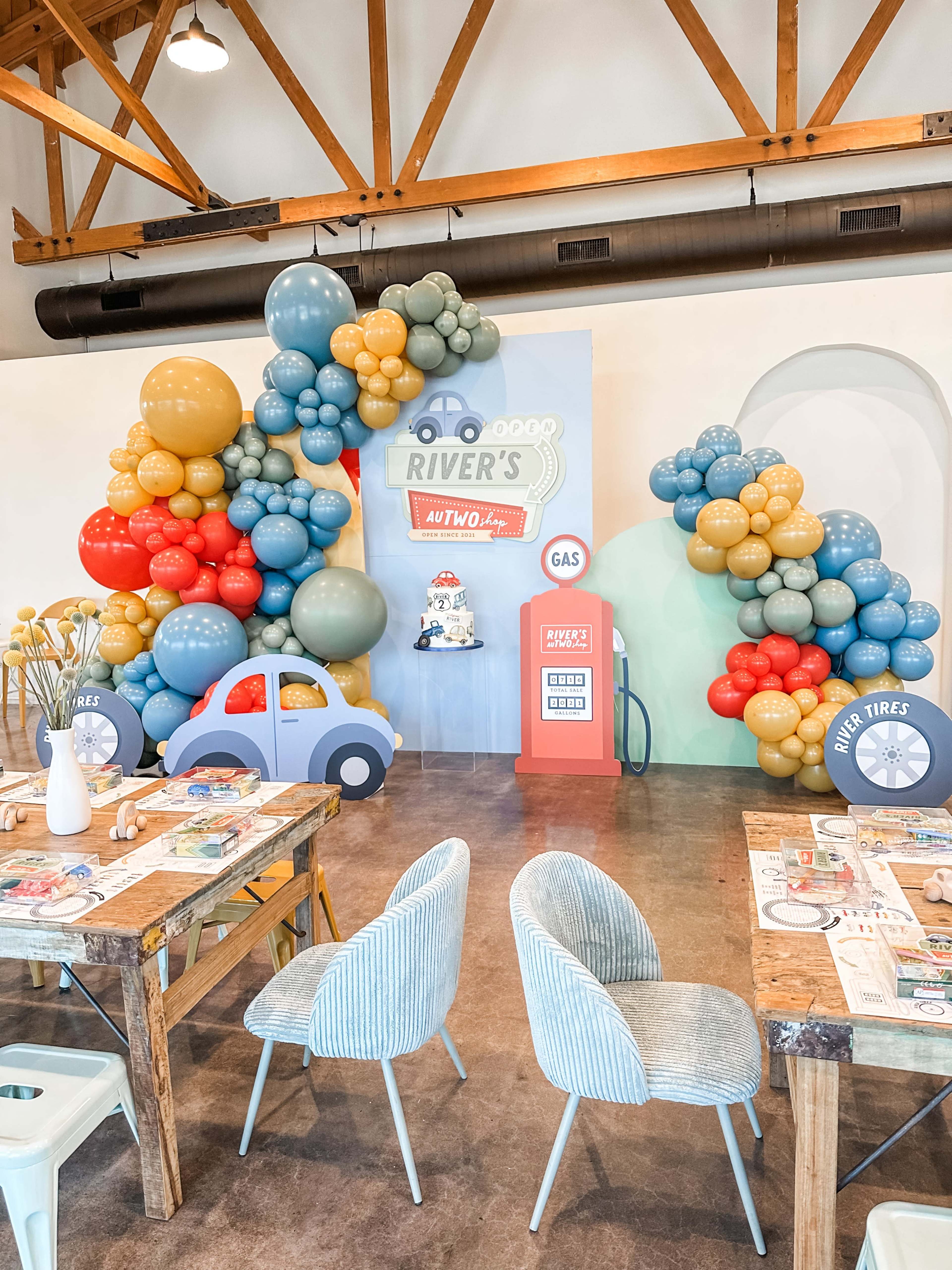 A festive scene featuring colorful balloon decorations in the shape of a car-themed auto repair shop, complete with a vintage gas pump, set up against a backdrop.
